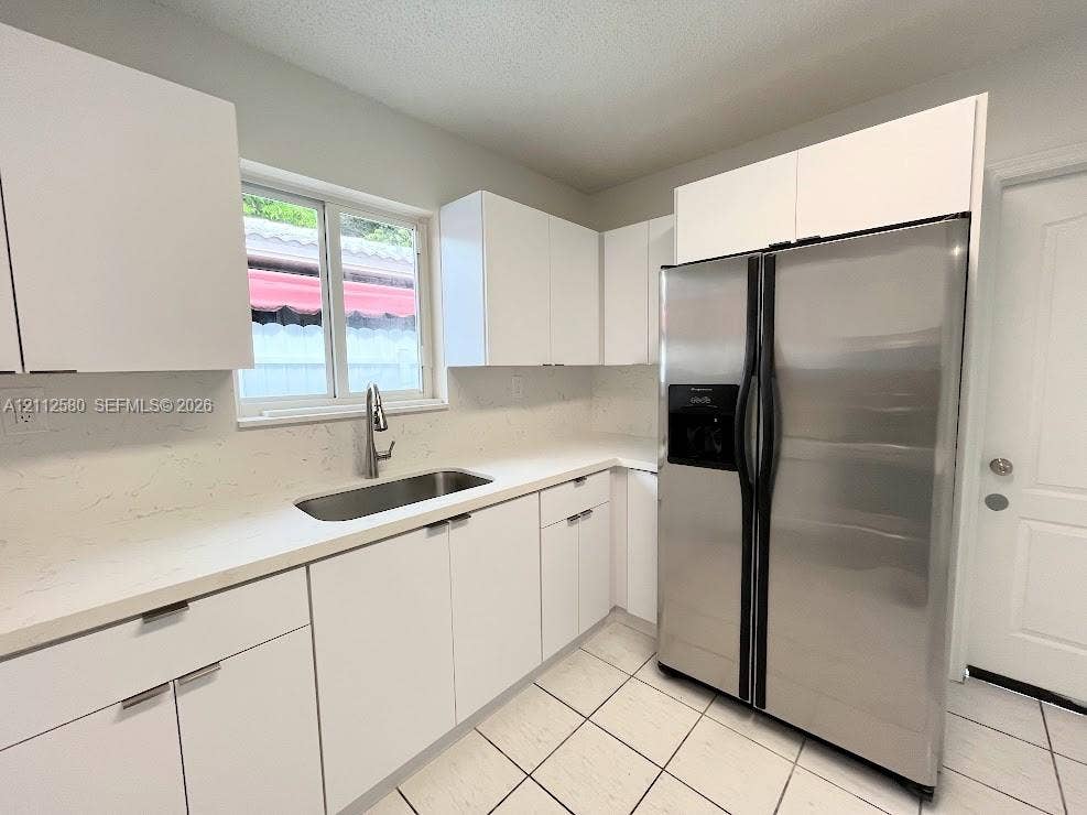 Kitchen featuring white flat-panel cabinetry, light-colored quartz countertops, stainless steel side-by-side refrigerator, under-mount sink with pull-down faucet, and tile flooring