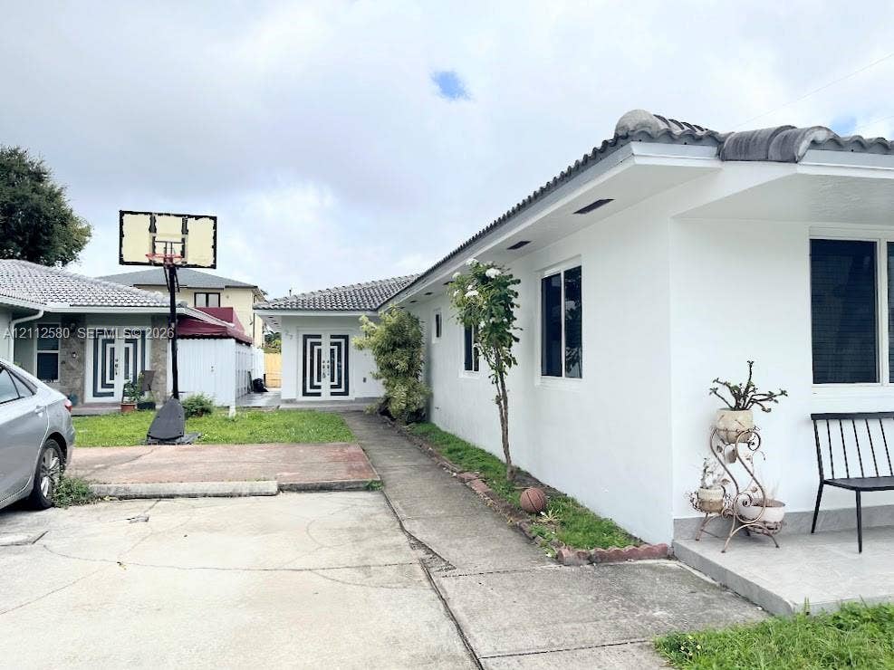 Exterior facade featuring a concrete tile roof, crisp white stucco finish, dual-entry doors with geometric detailing, and paved driveway space