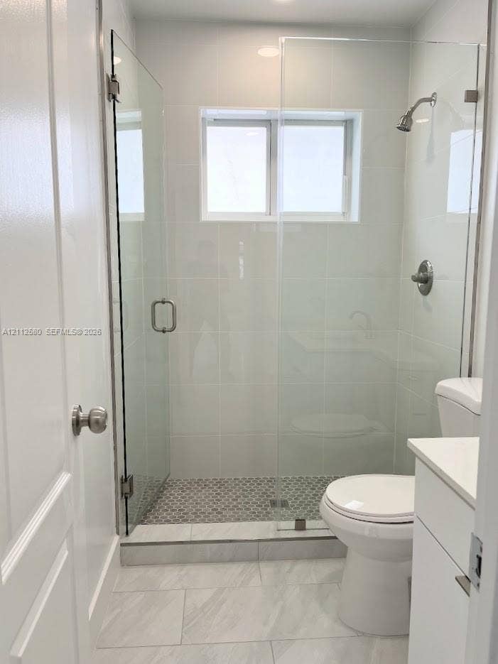 Walk-in shower featuring a frameless glass enclosure, polished chrome fixtures, white subway-style wall tile, and patterned tile flooring