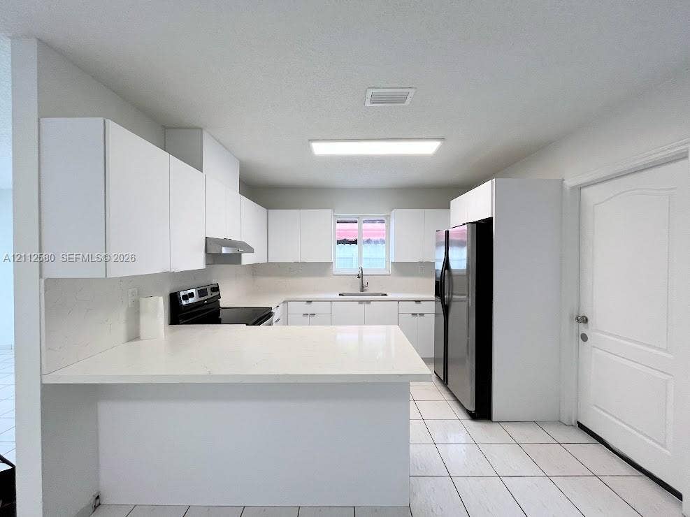 Kitchen featuring flat-panel white cabinetry, quartz countertops, tile flooring, and integrated black appliances
