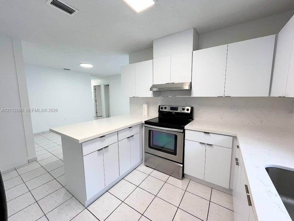 Kitchen featuring flat-panel white cabinetry, stone-finish countertops, stainless steel range with overhead hood, and tile flooring