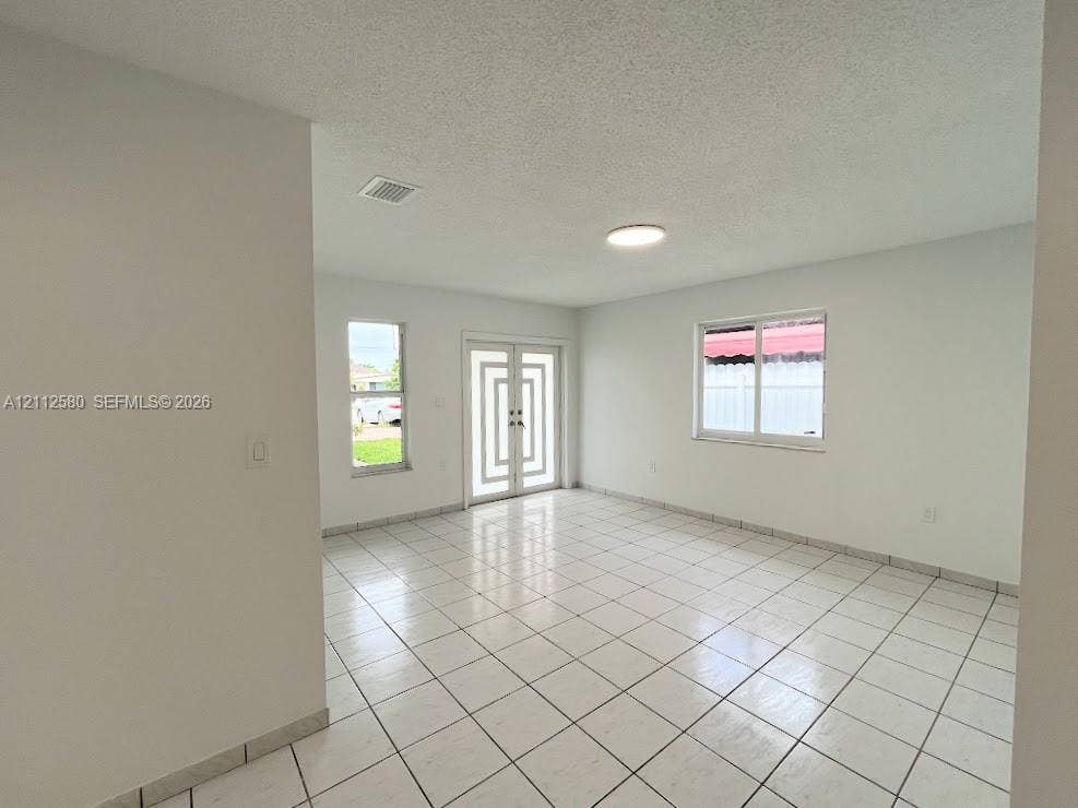 Interior space featuring white tile flooring, neutral walls, double front doors with geometric glass detailing, and dual-pane windows