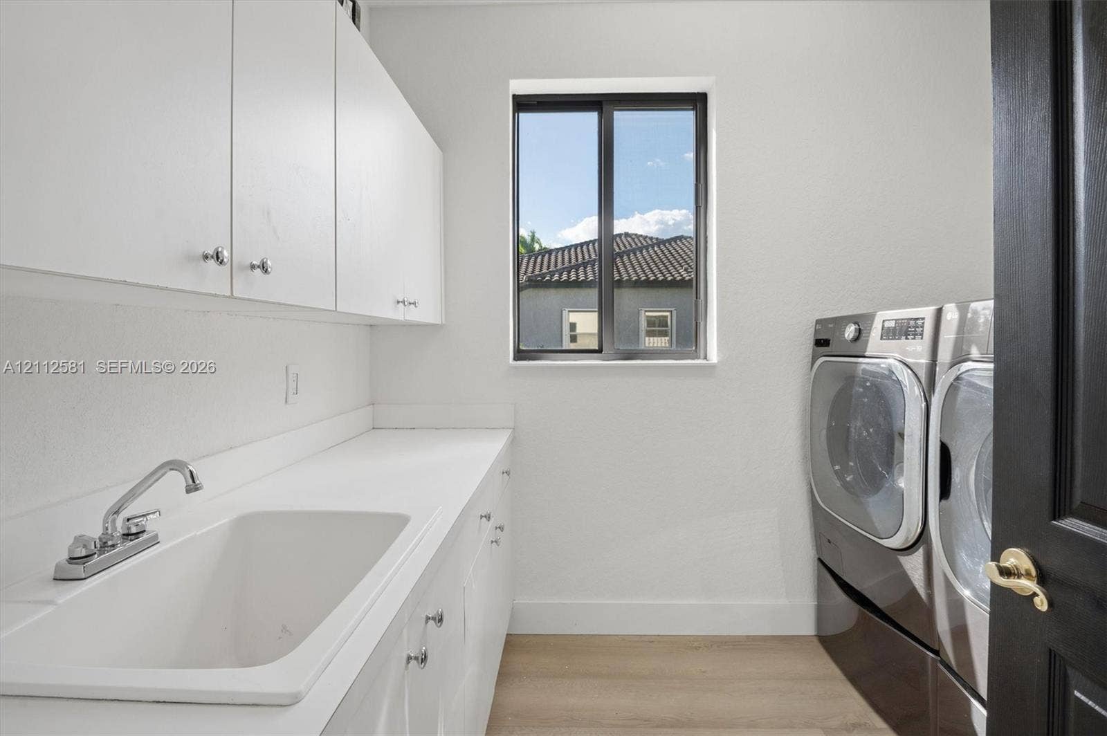 Laundry space featuring custom white cabinetry, a built-in utility sink with a chrome faucet, solid-surface countertops, and wood-finish flooring