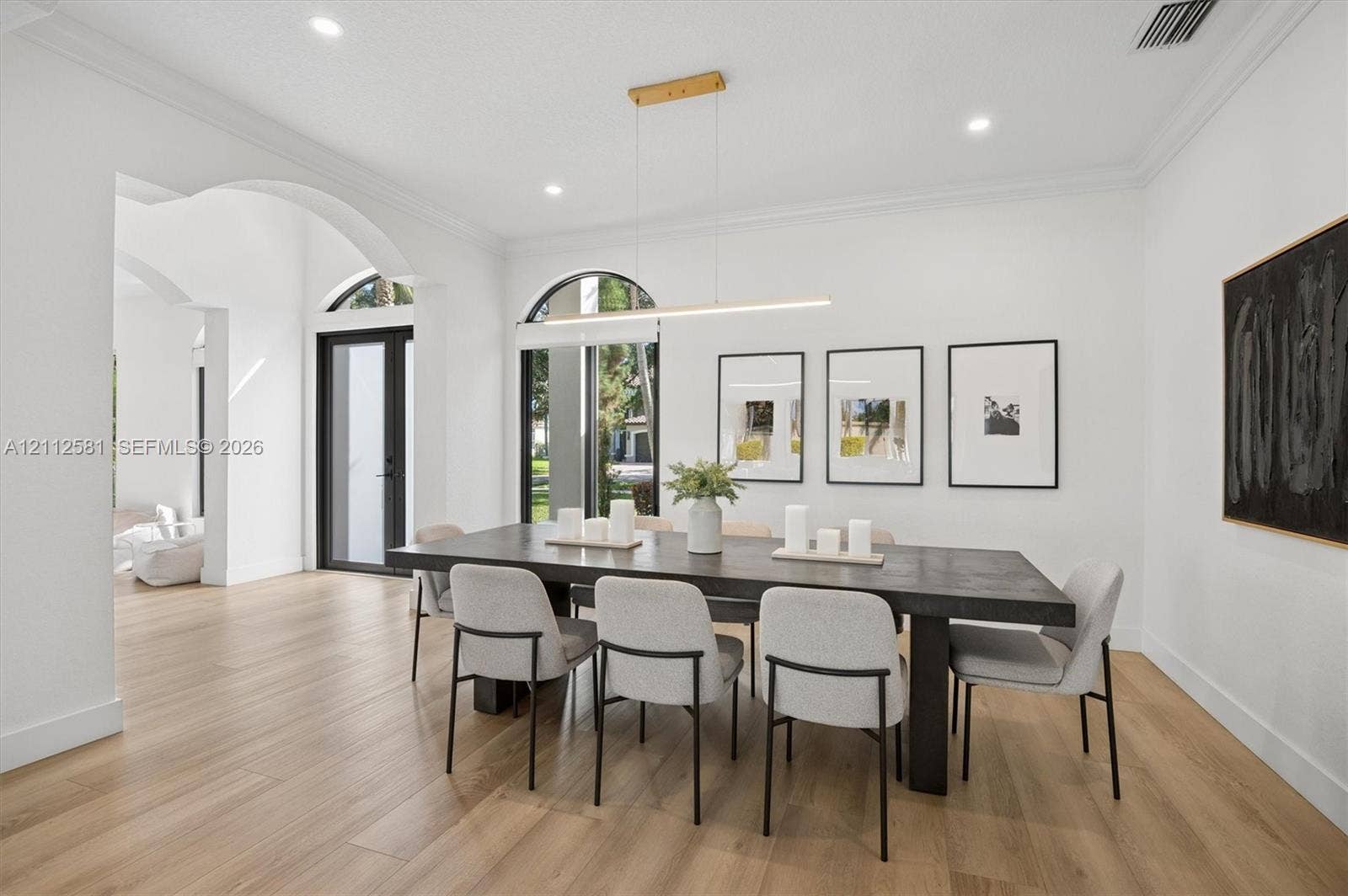 Dining space featuring wood-finish flooring, arched windows, crown molding, recessed lighting, and a modern linear pendant fixture