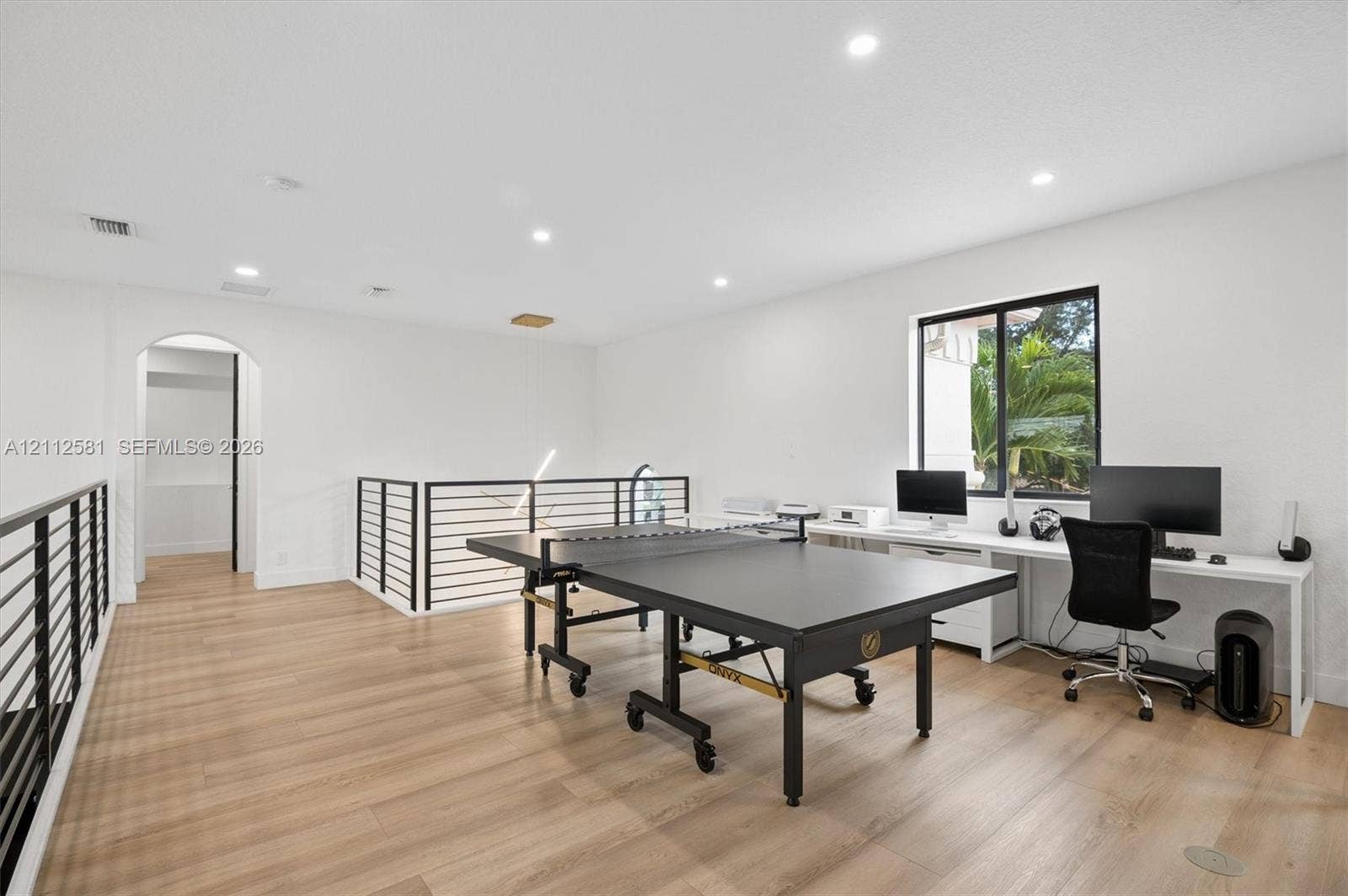 Open-concept space featuring wood-finish flooring, recessed lighting, a built-in white desk, and matte black metal railings