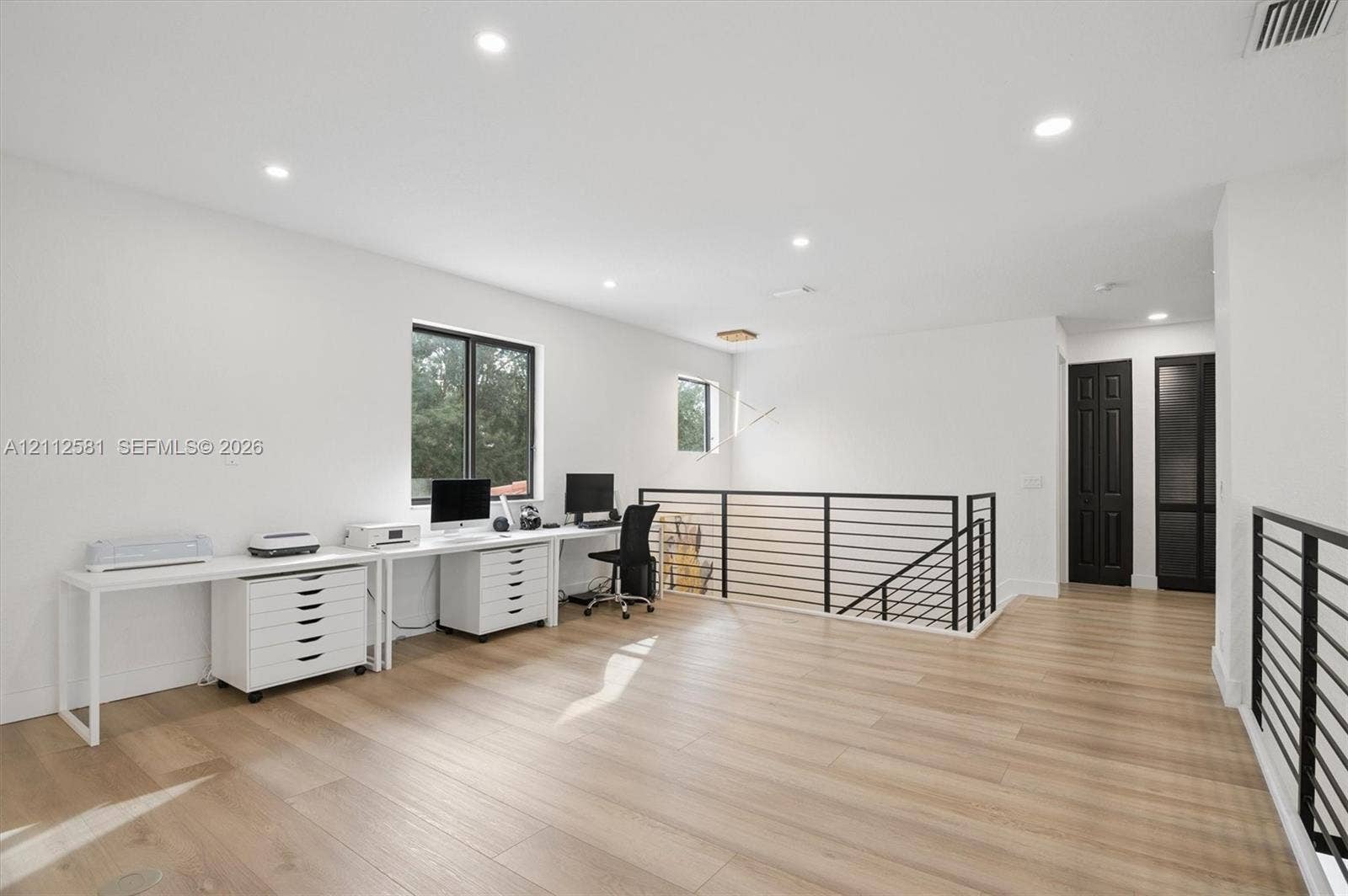 Open-concept landing featuring wood-finish flooring, recessed lighting, matte black metal railings, and dual dark-finish doors