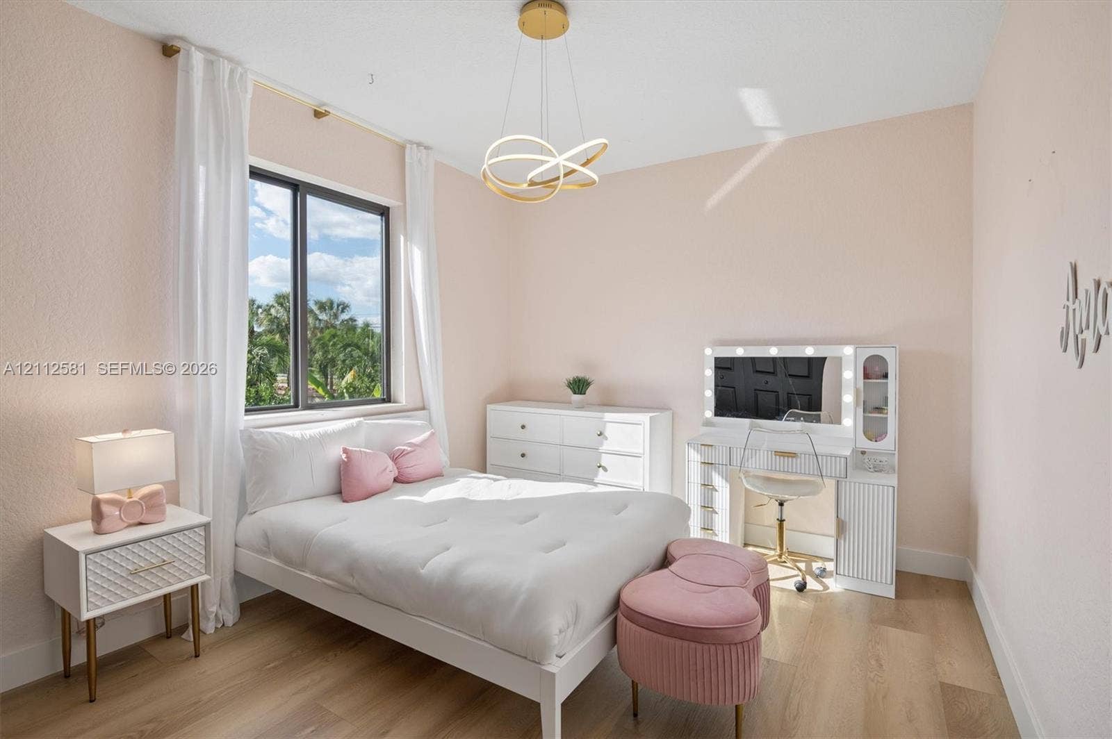 Bedroom featuring wood-finish flooring, a large window with exterior tropical scenery, and a modern gold-finish geometric pendant light