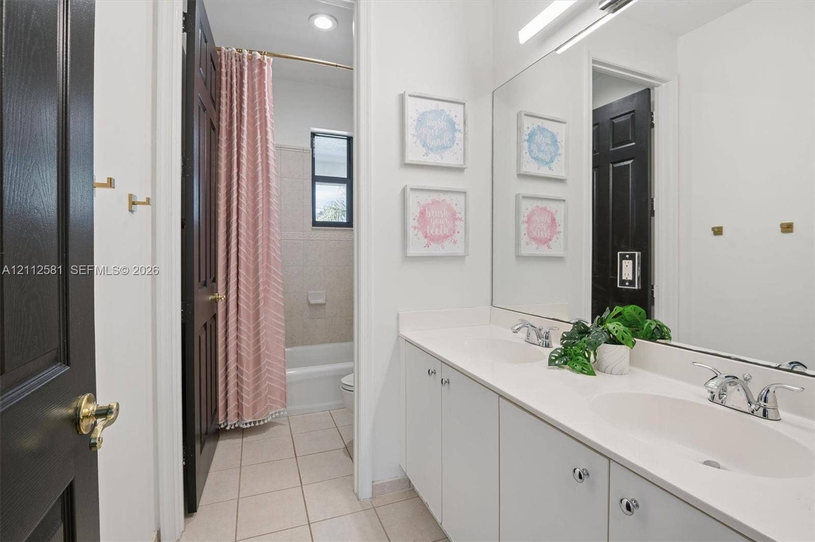 Dual-sink vanity with a solid-surface countertop and chrome-finish hardware, paired with a full-width wall mirror and tile flooring