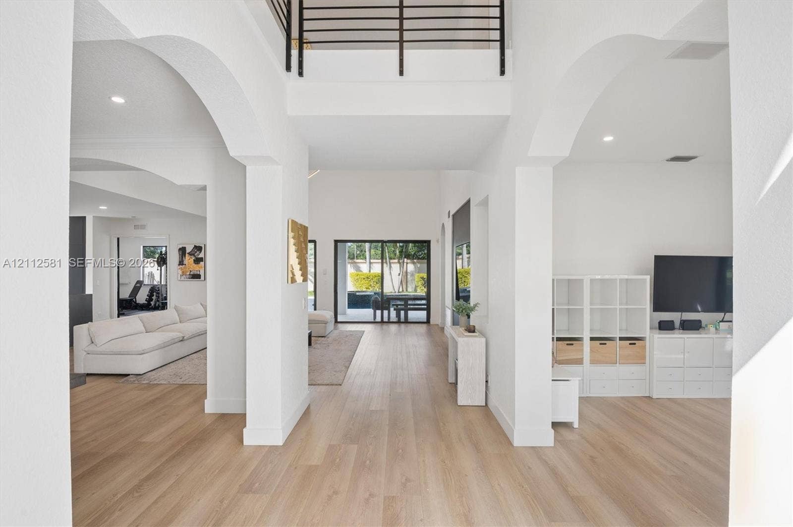 Double-height entryway featuring arched architectural detailing, wood-finish flooring, recessed lighting, and a metal staircase railing