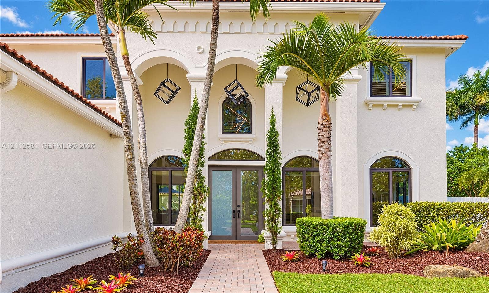 Mediterranean-style exterior featuring a covered entryway with structural arches, decorative pendant lighting, arched window accents, and a paved walkway