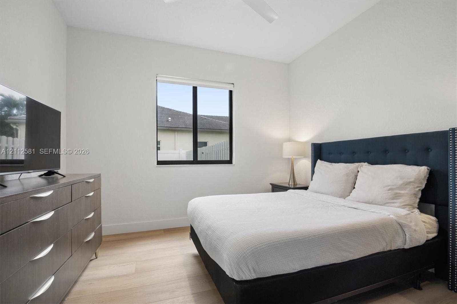 Neutral walls, wood-finish flooring, ceiling fan, and single-pane window with black framing