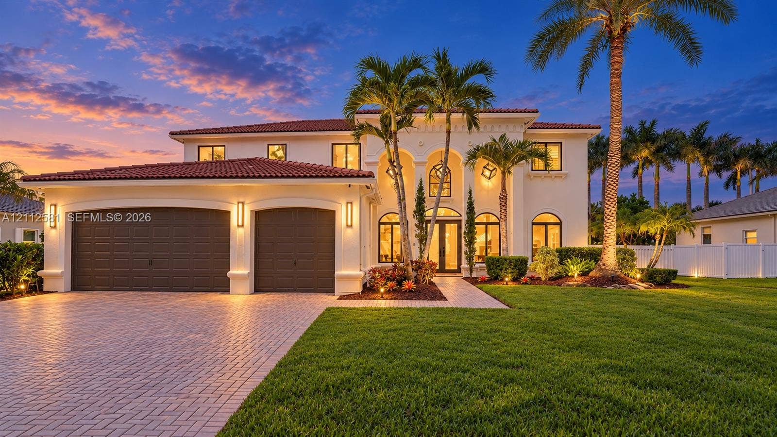 Mediterranean-style exterior featuring a clay tile roof, arched entryway, stucco facade, paved driveway, and integrated outdoor wall lighting