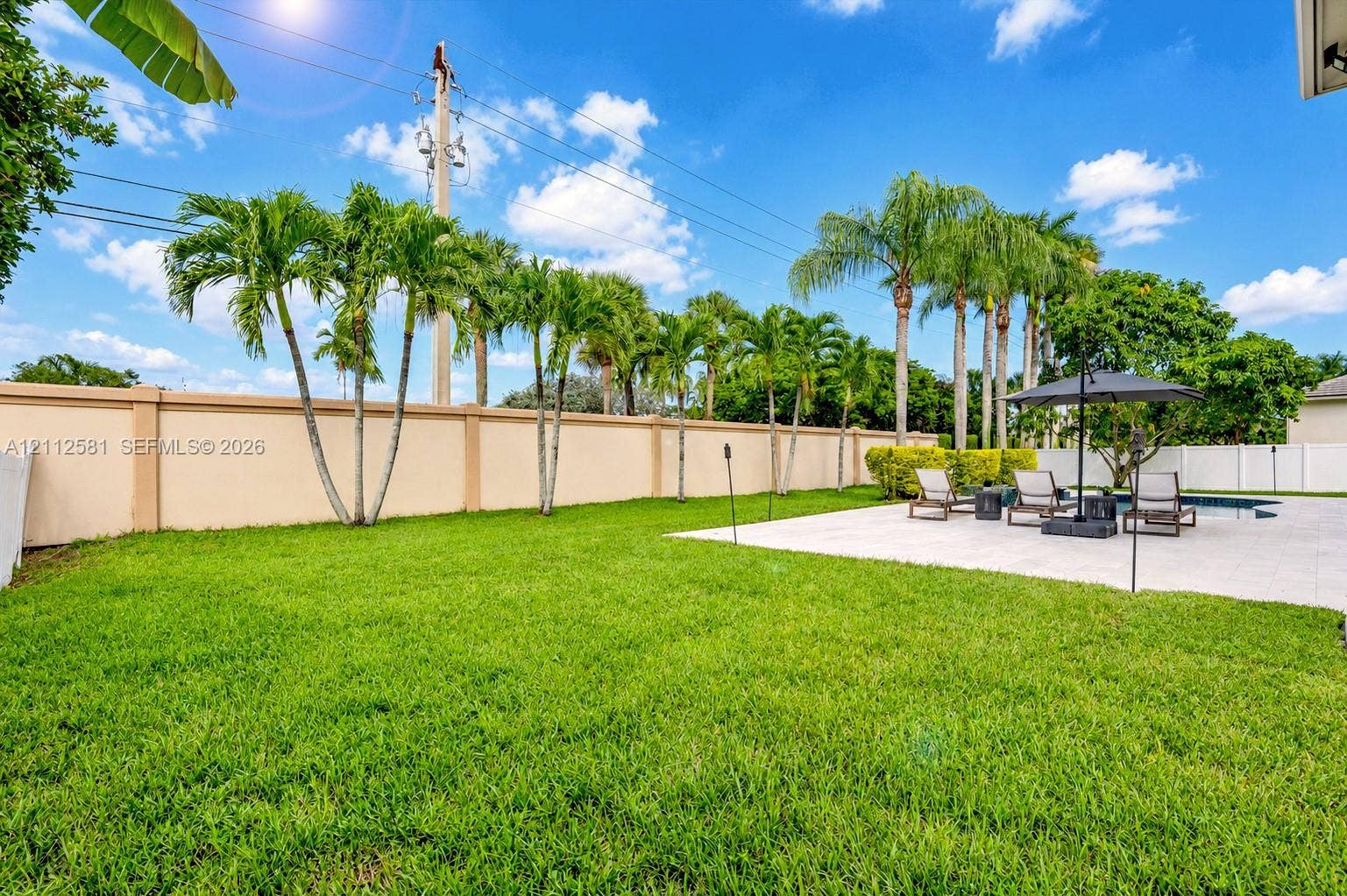 Private backyard featuring a manicured lawn, concrete paver patio, in-ground swimming pool, and concrete masonry perimeter wall