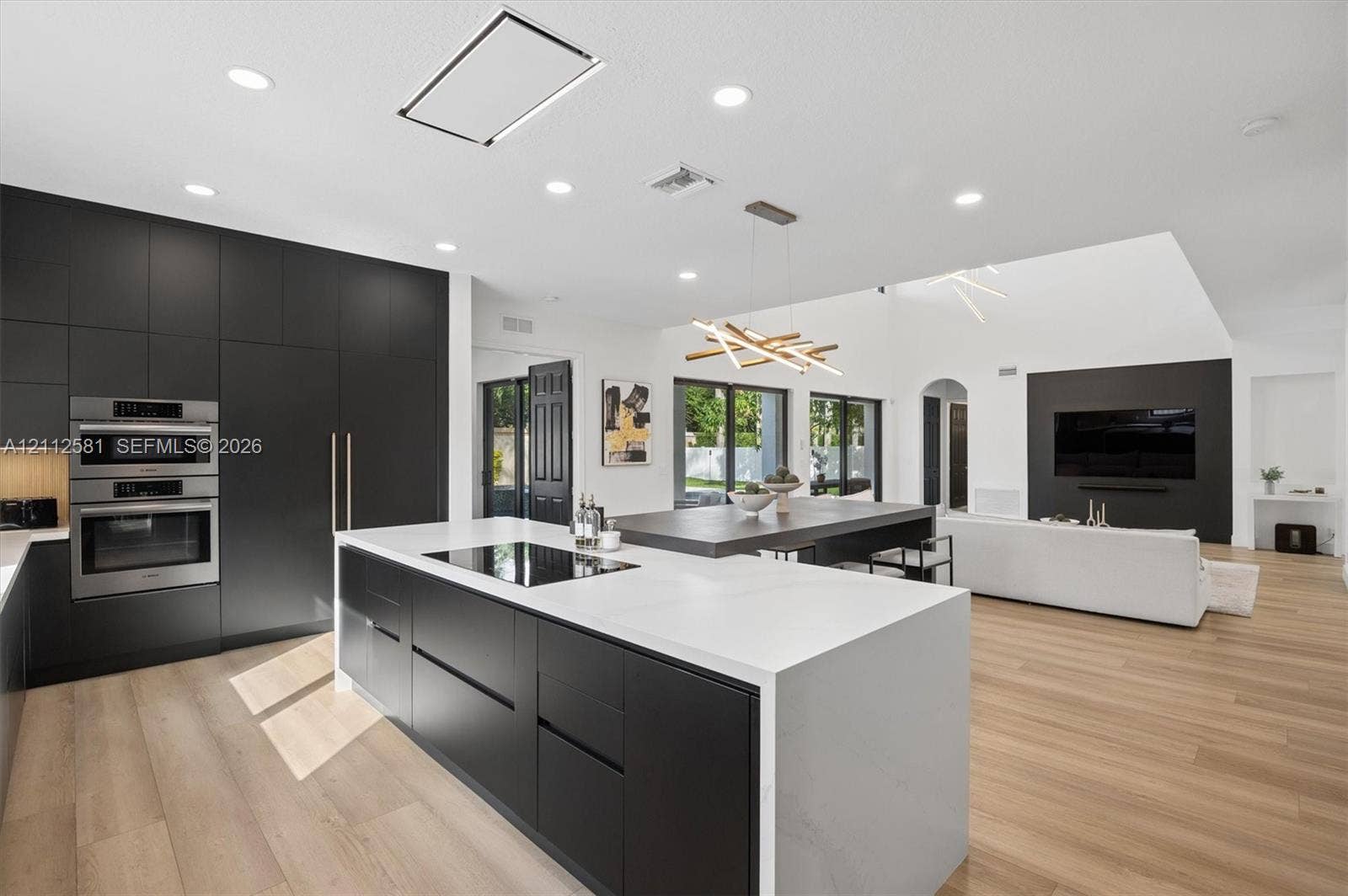Kitchen featuring matte black floor-to-ceiling cabinetry, a central island with a waterfall-edge countertop, wood-finish flooring, recessed lighting, and stainless-steel built-in appliances