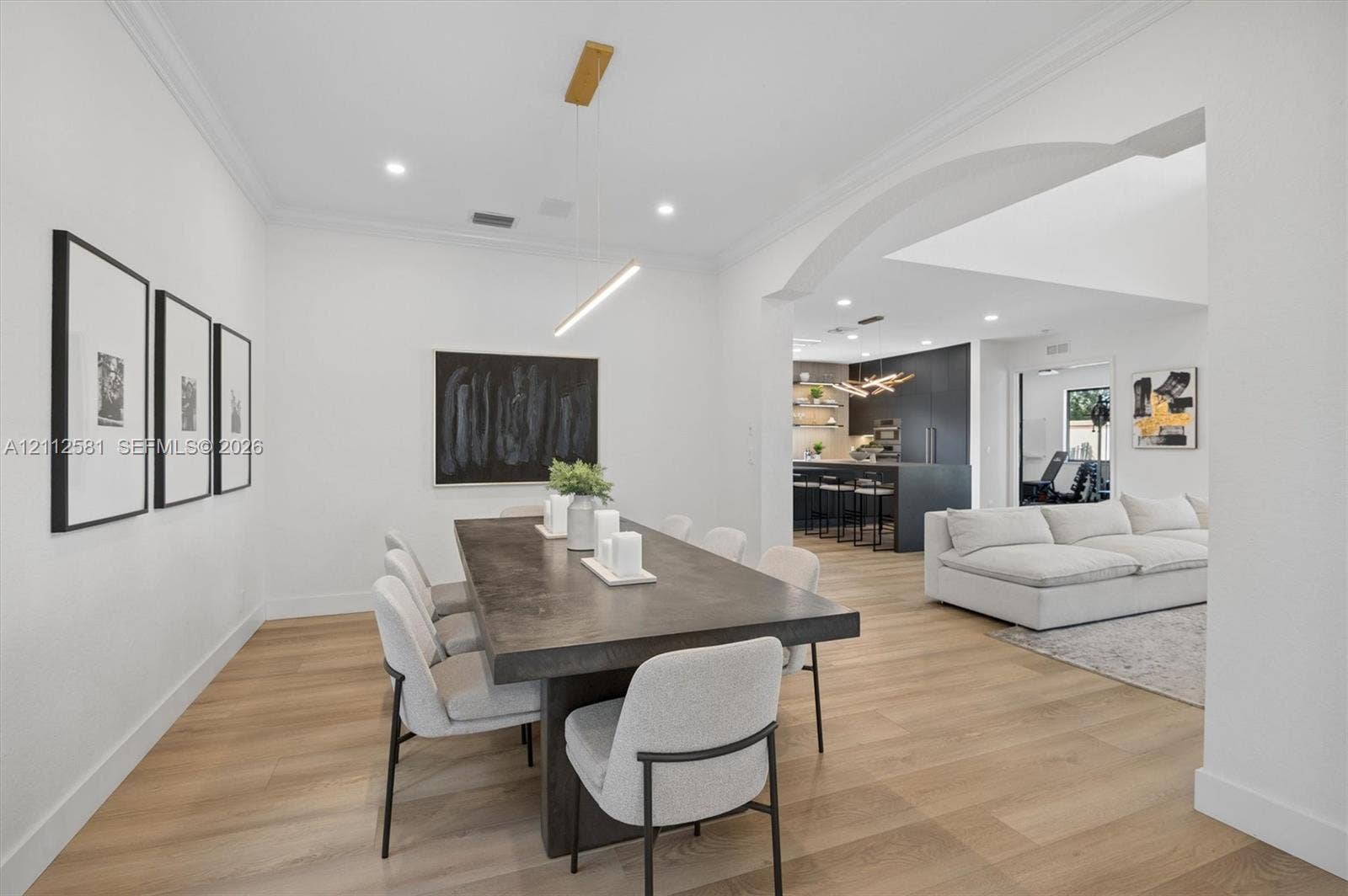 Dining area featuring wood-finish flooring, crown molding, a linear pendant light fixture, and an arched entry