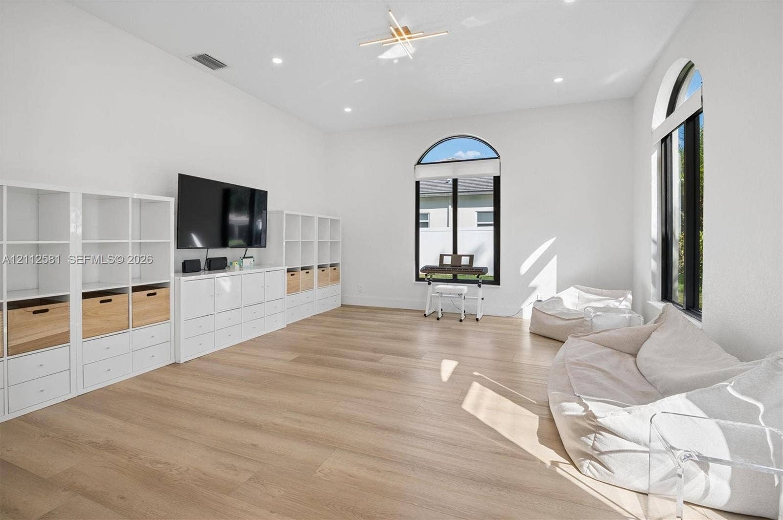 Spacious room featuring high ceilings, wood-finish flooring, recessed lighting, arched windows with black frames, and a modern tiered geometric ceiling fixture