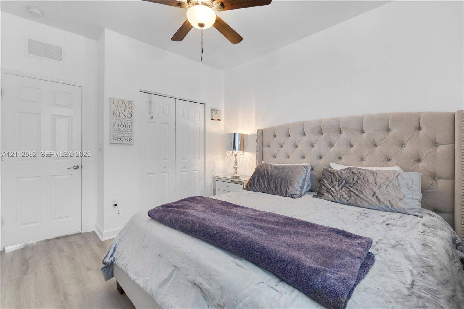 Wood-finish flooring, white panel door, double-door closet with bifold access, and a ceiling fan with integrated light fixture