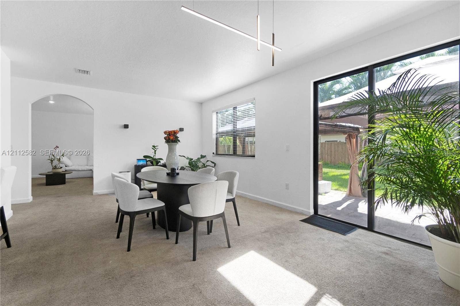 Open-concept room featuring floor-to-ceiling sliding glass doors, minimalist linear pendant lighting, an arched architectural doorway, and wall-mounted sconces