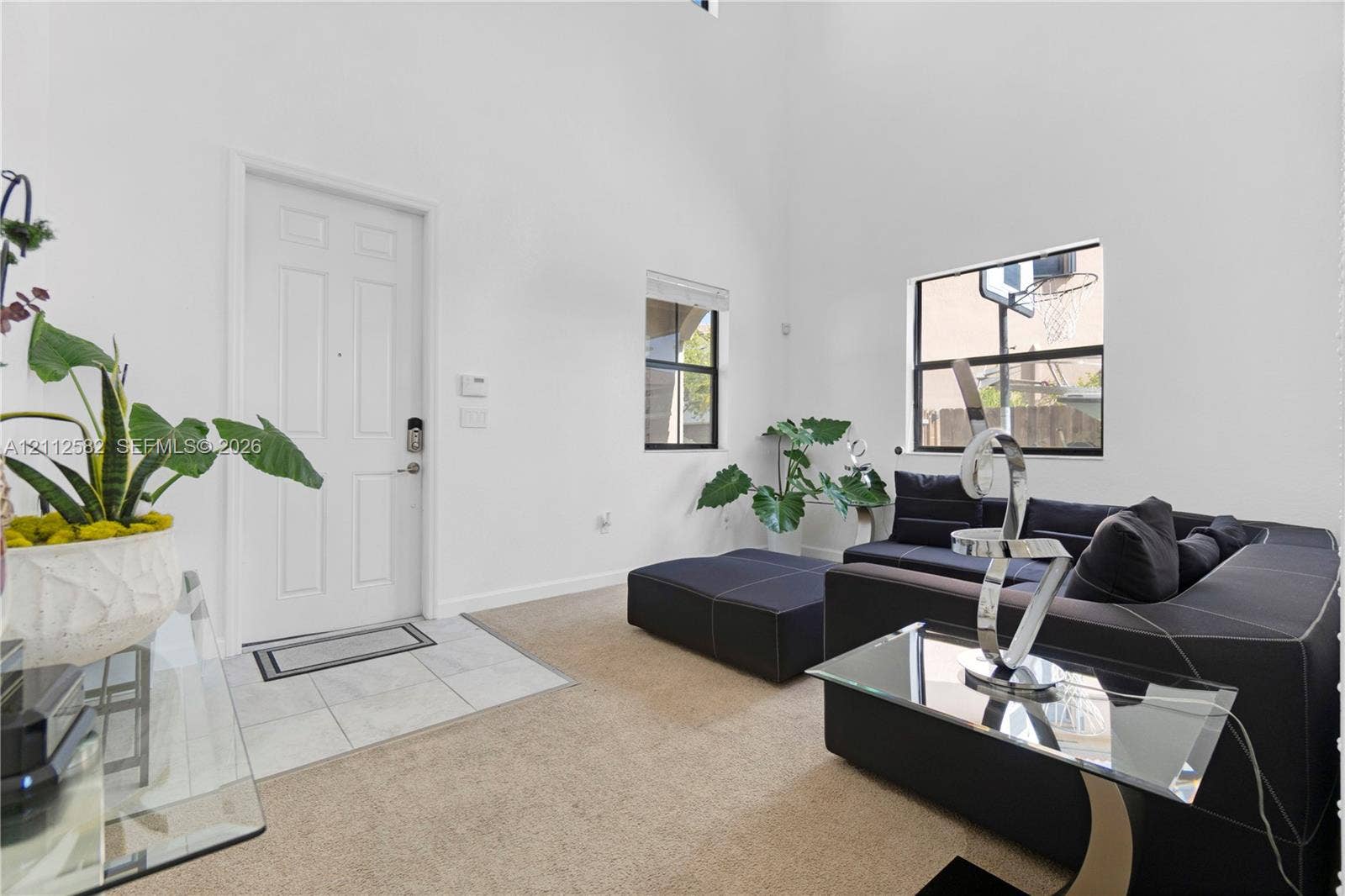 High-ceiling living area featuring neutral carpeting, ceramic tile entryway flooring, and large window placements