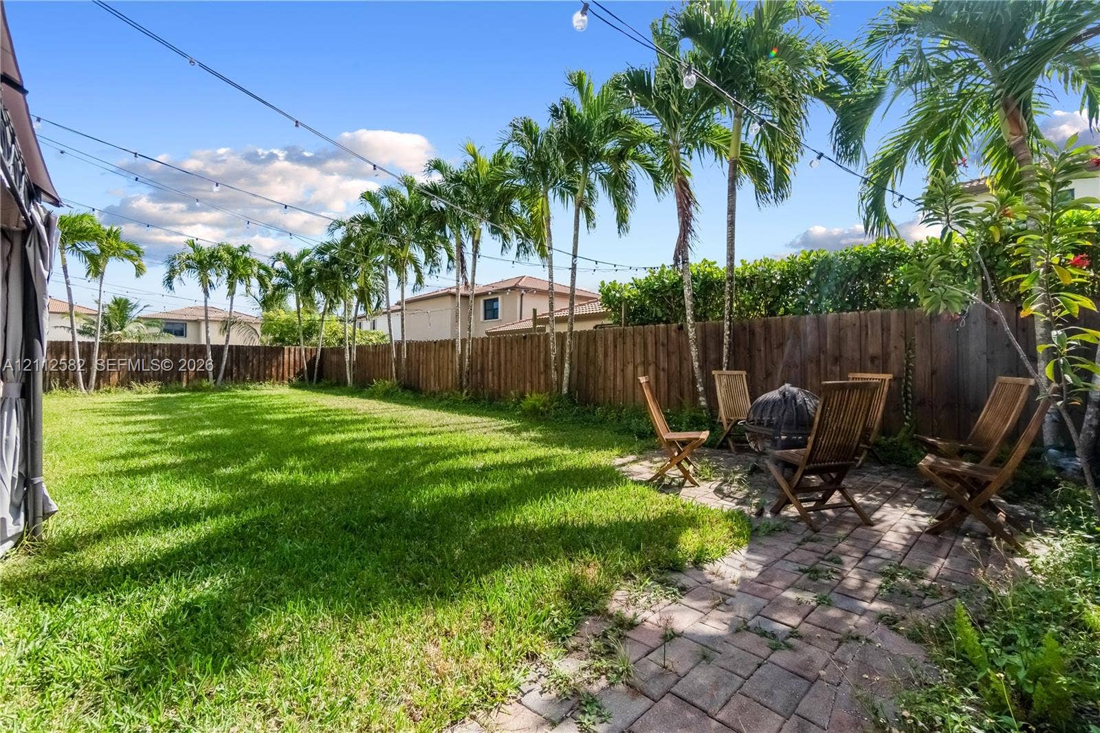 Expansive backyard featuring a manicured lawn, paver patio, tall perimeter wood fencing, and mature palm trees