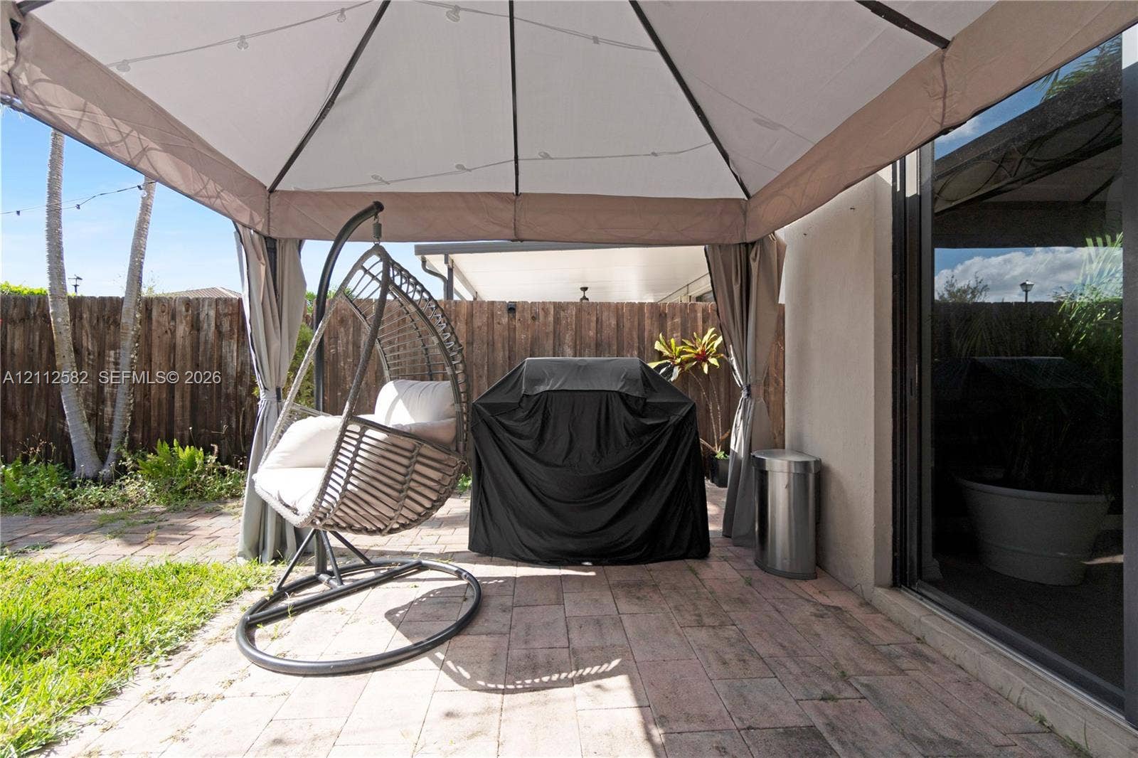 Rear patio featuring paved stone flooring, a fabric-topped gazebo, and a perimeter wood-plank privacy fence