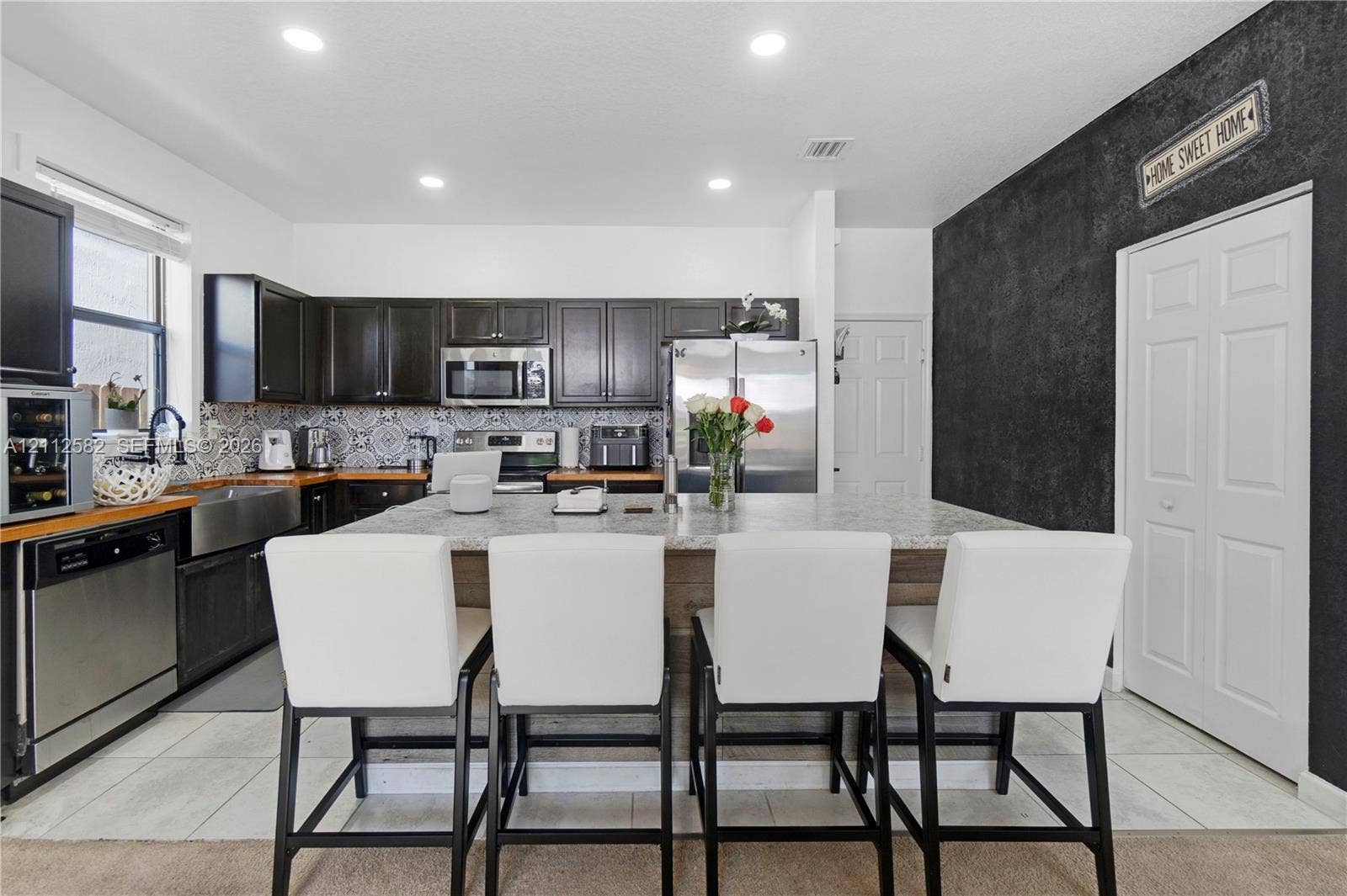 Kitchen featuring dark wood cabinetry, stainless steel appliances, patterned tile backsplash, oversized stone-topped island, and recessed lighting