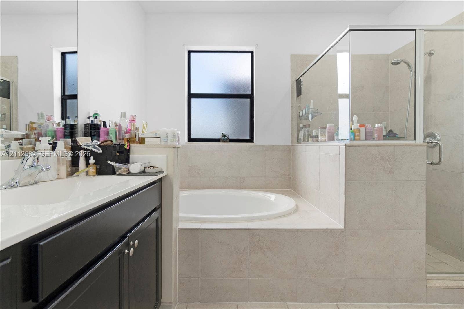 Bathroom featuring a dark wood-finish vanity, solid-surface countertop with an integrated basin, a large soaking tub, and a walk-in shower with tile surround and glass enclosure