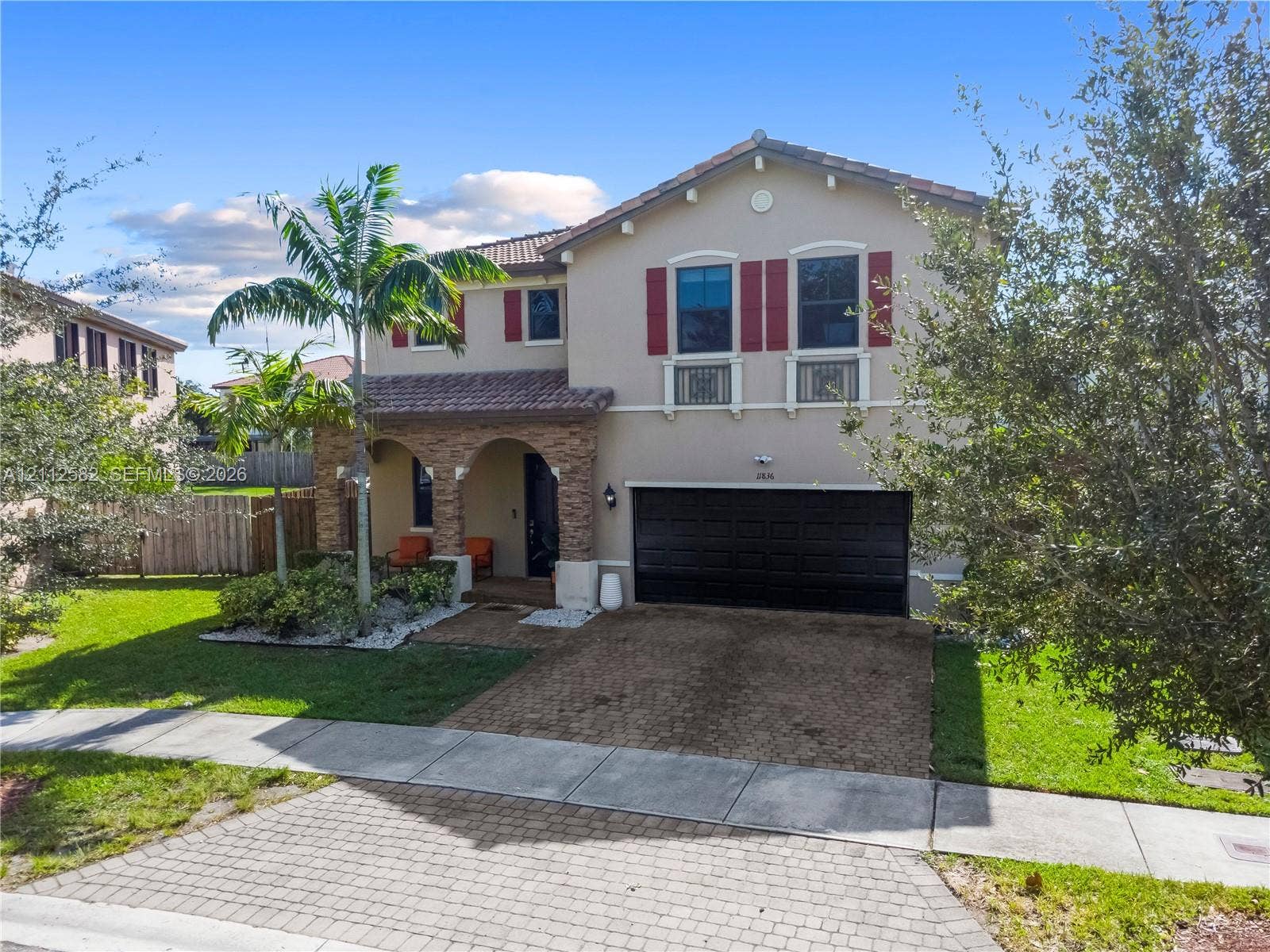 Two-story stucco exterior featuring arched entryway masonry, decorative red shutters, wrought iron balcony railings, and a two-car garage