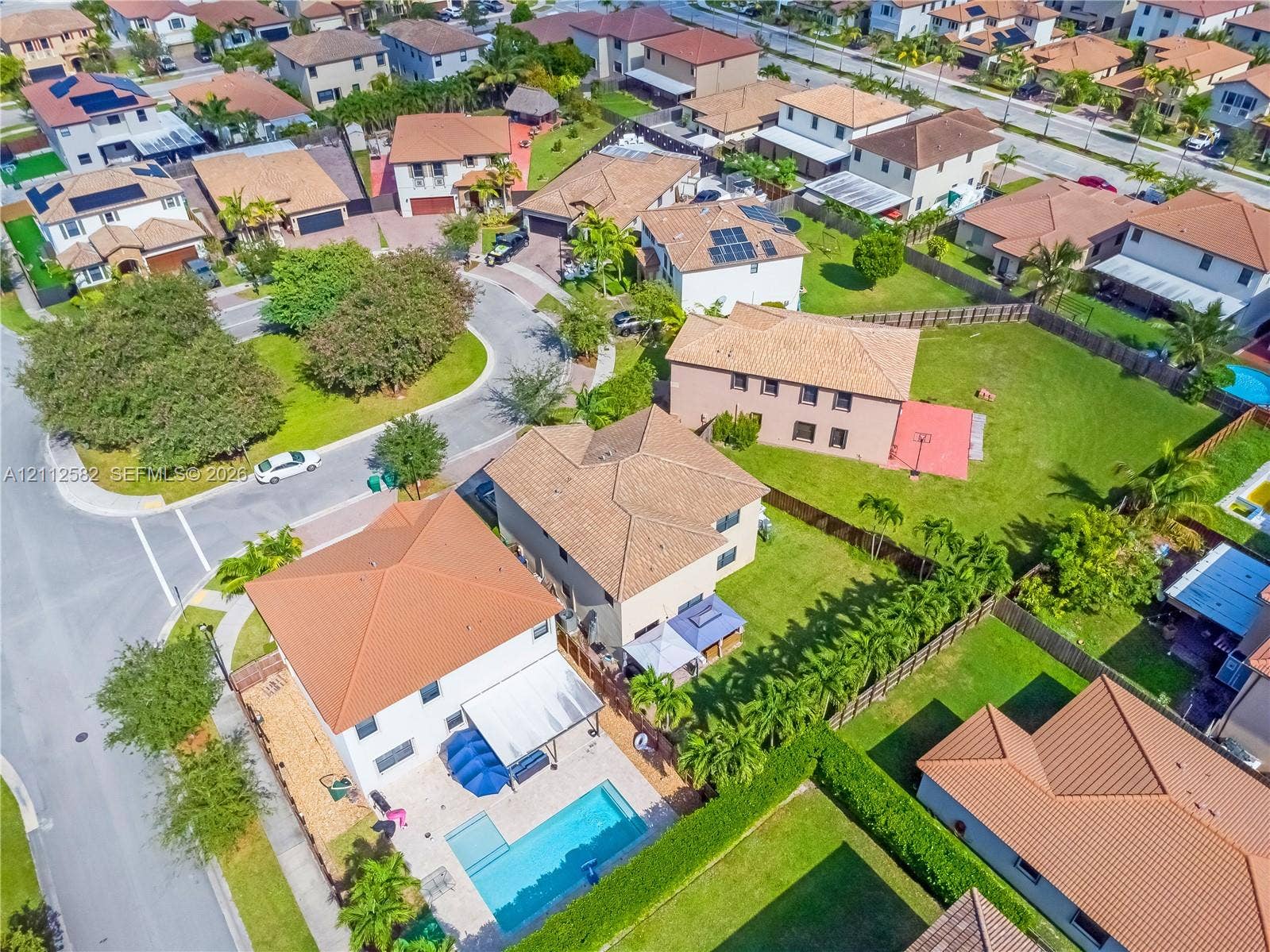 Aerial perspective of a multi-story residence featuring a rectangular swimming pool, concrete pool deck, and perimeter fencing