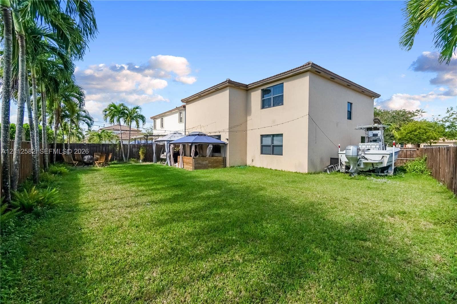 Expansive backyard featuring a manicured lawn, mature palm trees, and wood-panel perimeter fencing