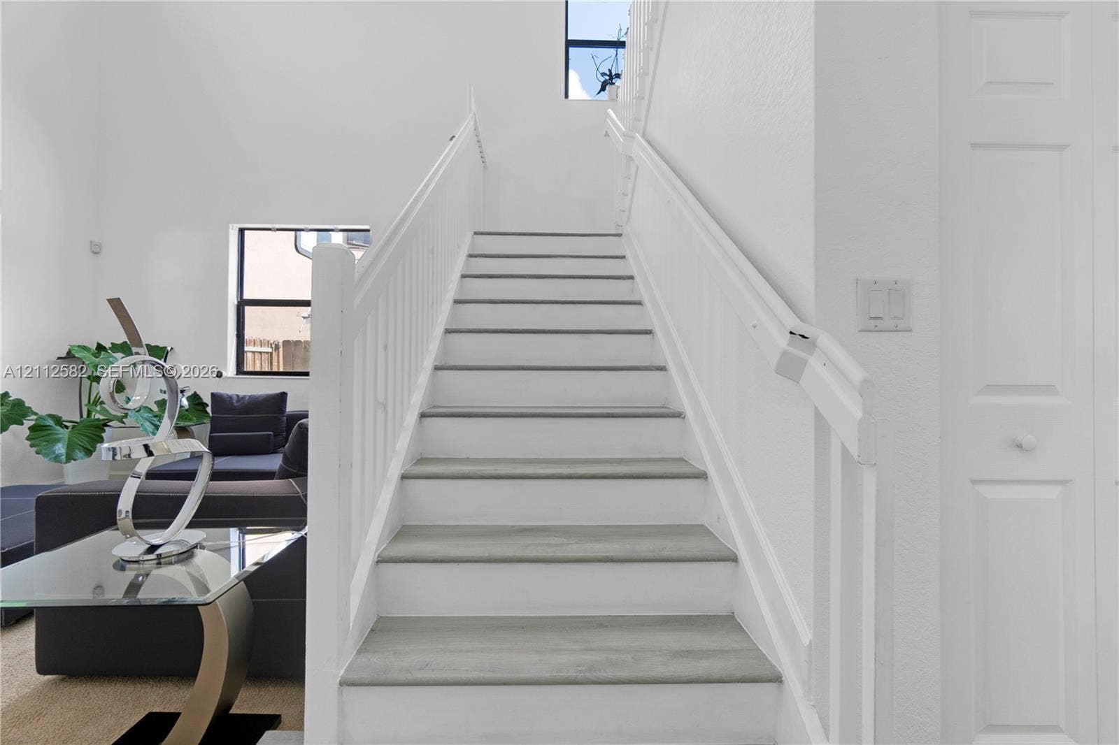 Staircase featuring wood-finish treads, white risers, and white balustrade with a matching handrail, set against a soaring vaulted ceiling