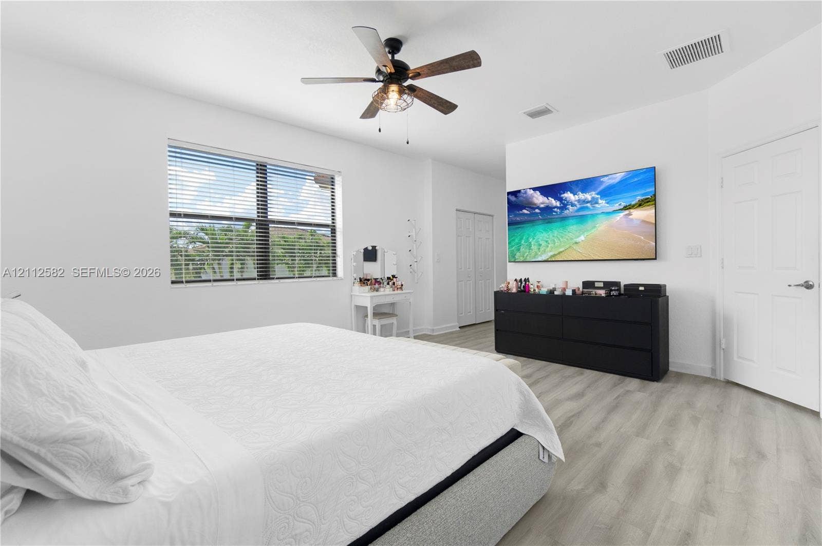 Neutral-toned interior space featuring wood-finish flooring, a multi-blade ceiling fan with integrated lighting, and a multi-pane window