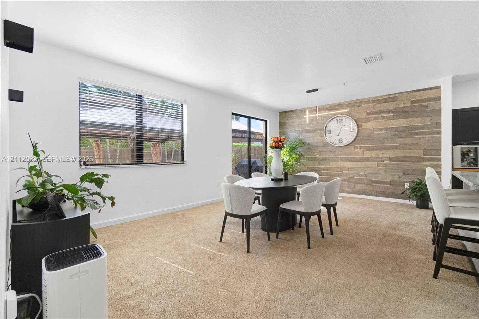 Dining area featuring a wood-plank accent wall, linear pendant lighting, neutral carpeting, and a glass sliding door