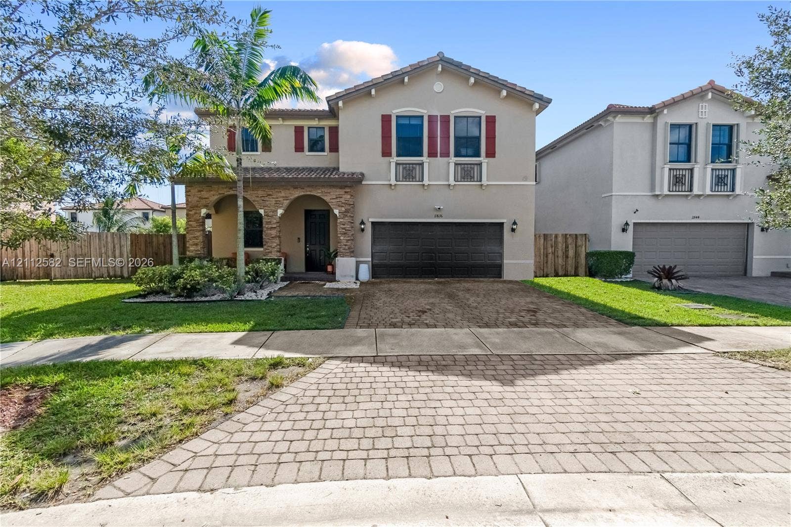 Two-story residence featuring a stone-clad arched entryway, paver driveway, decorative window shutters, and a multi-car garage