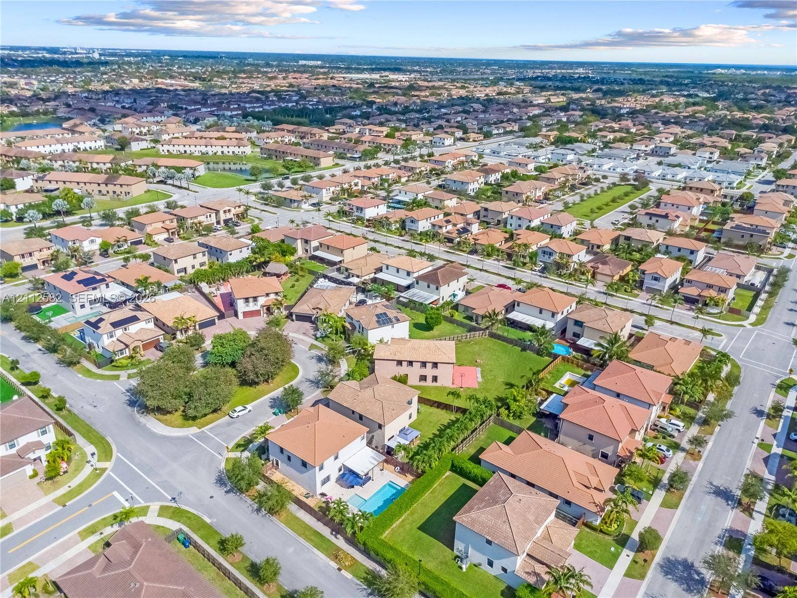 Aerial perspective of a suburban neighborhood featuring paved street infrastructure, multi-level residential homes with tiled roofs, private swimming pools, and manicured landscaping