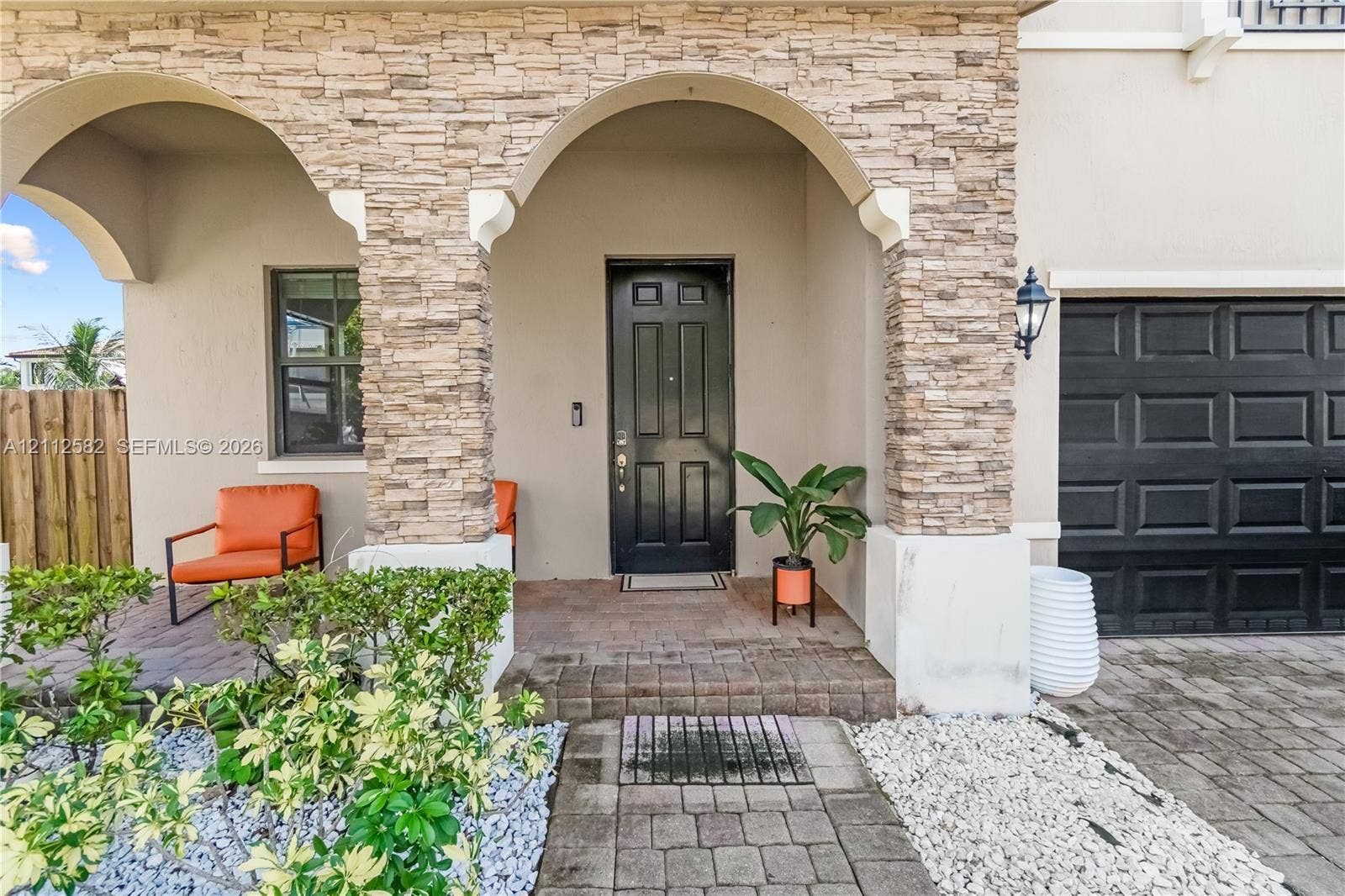 Exterior entry featuring stacked stone pillars, arched portico, paver walkway, and dark-toned entry door and garage