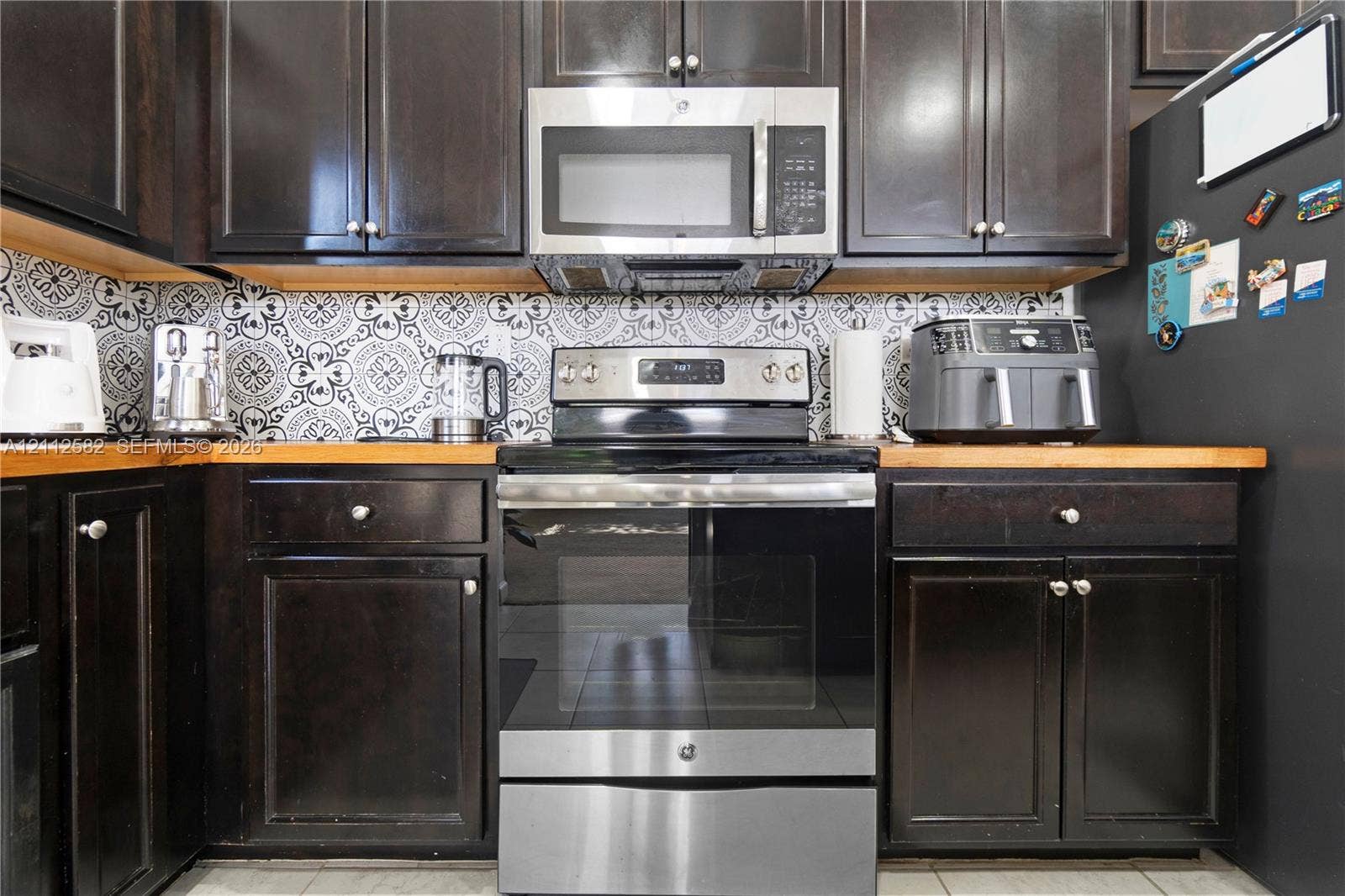 Dark-finish cabinetry, stainless steel oven and microwave, butcher-block countertops, and patterned tile backsplash