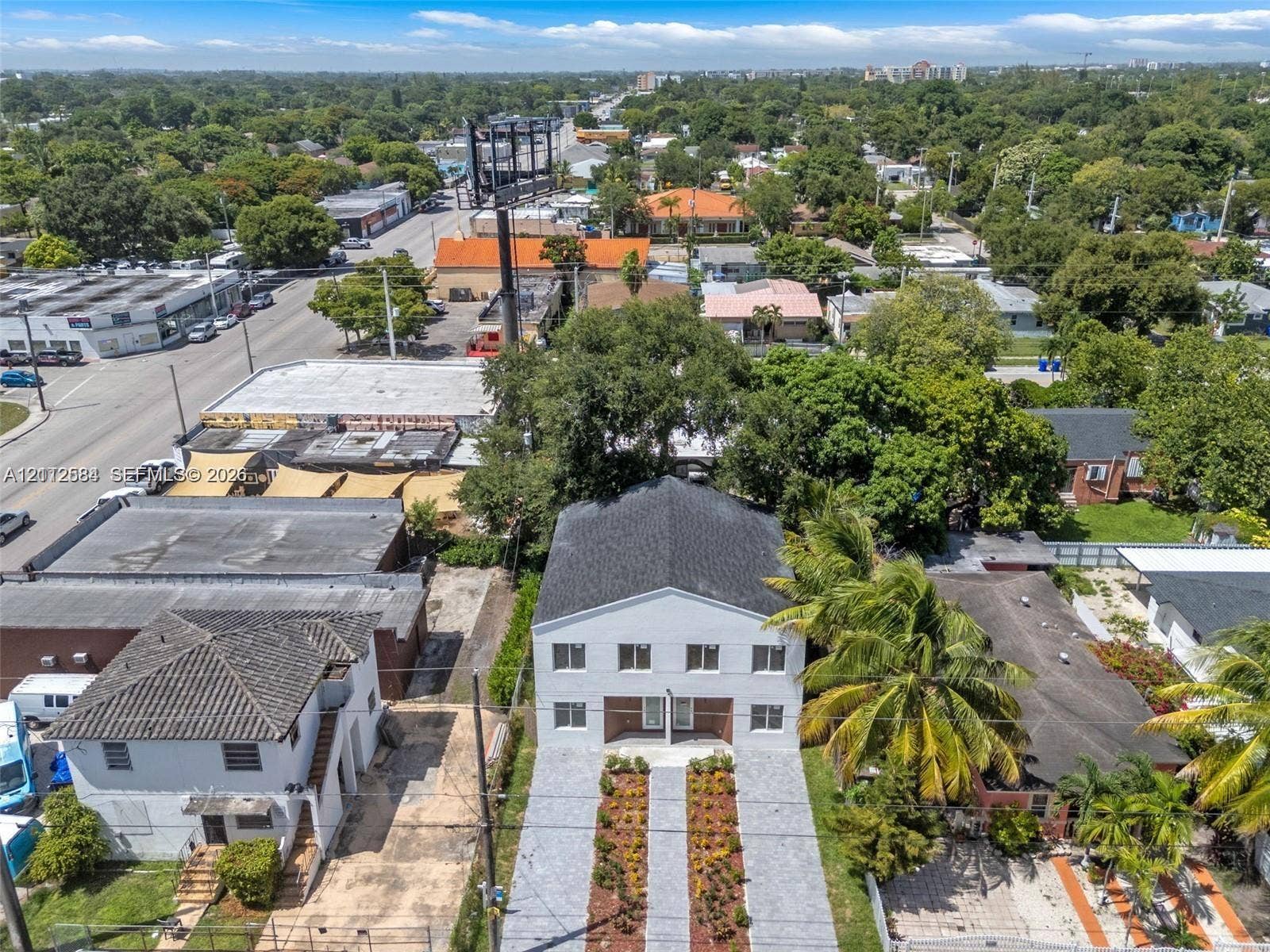 1629 NW 40th Street, Miami, FL 33142 Two-story multi-unit building featuring a white facade, gabled roof, paved dual-track driveway, and curated landscaping