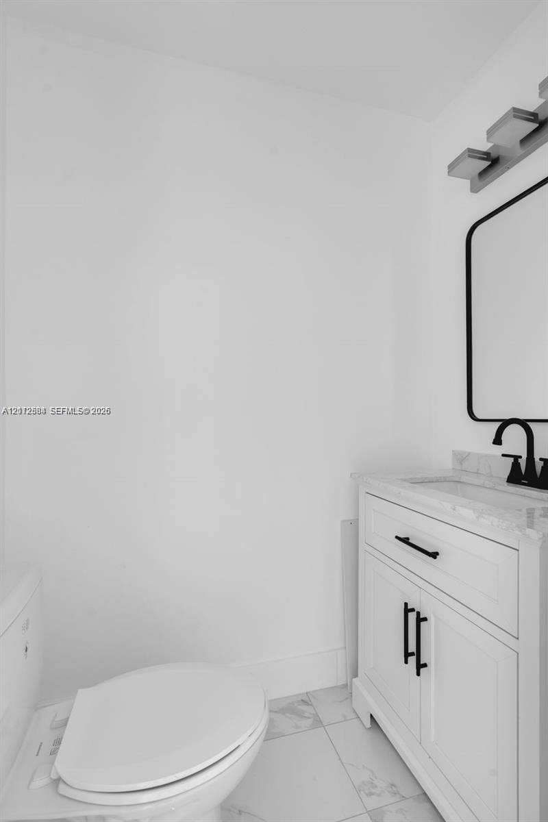 1629 NW 40th Street, Miami, FL 33142 White vanity with a stone countertop, under-mount sink, matte black faucet, matching hardware, and a framed mirror