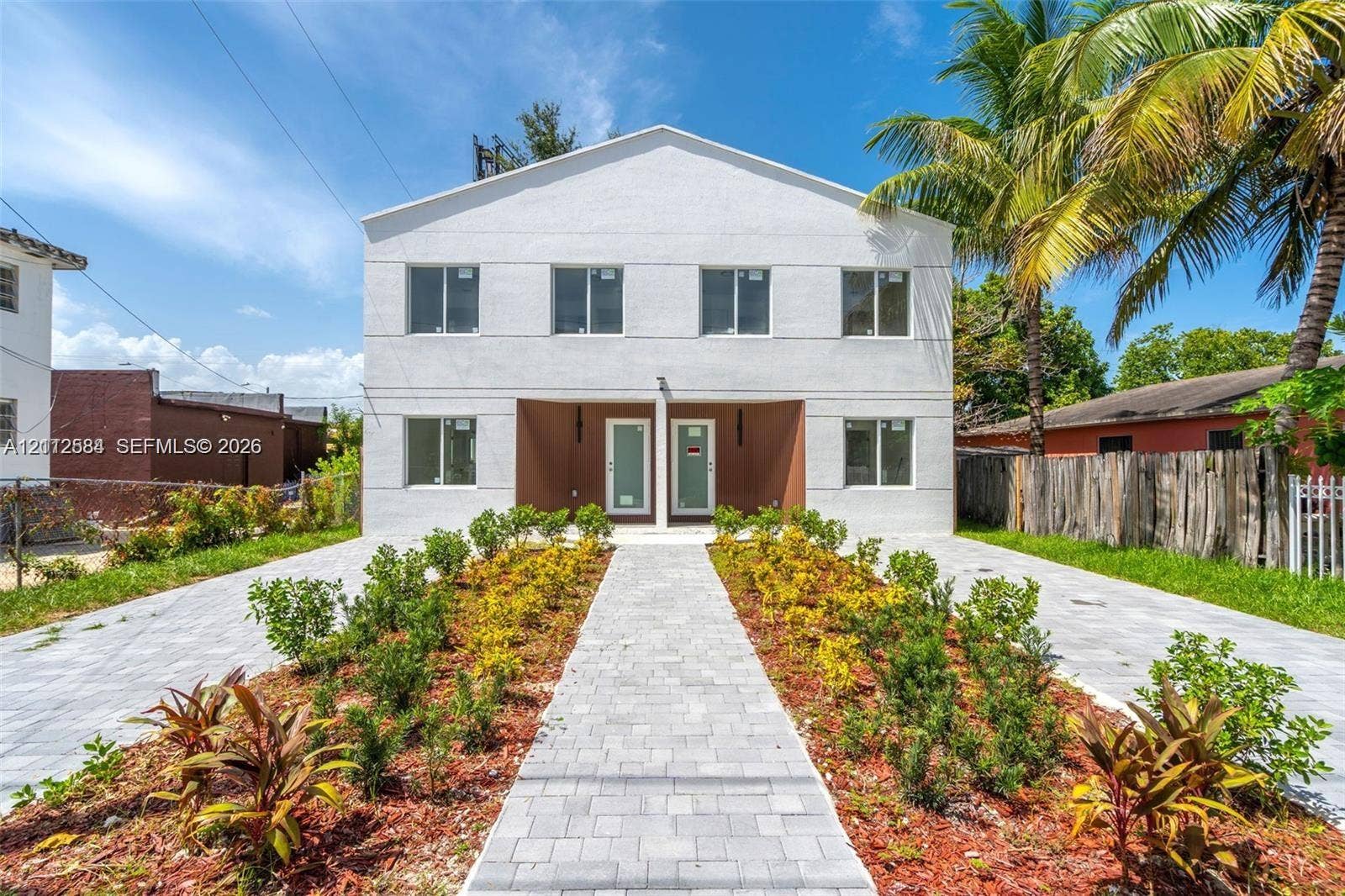 1629 NW 40th Street, Miami, FL 33142 Two-story exterior featuring a white stucco facade, paved walkways, landscaped garden beds, and dual entry points