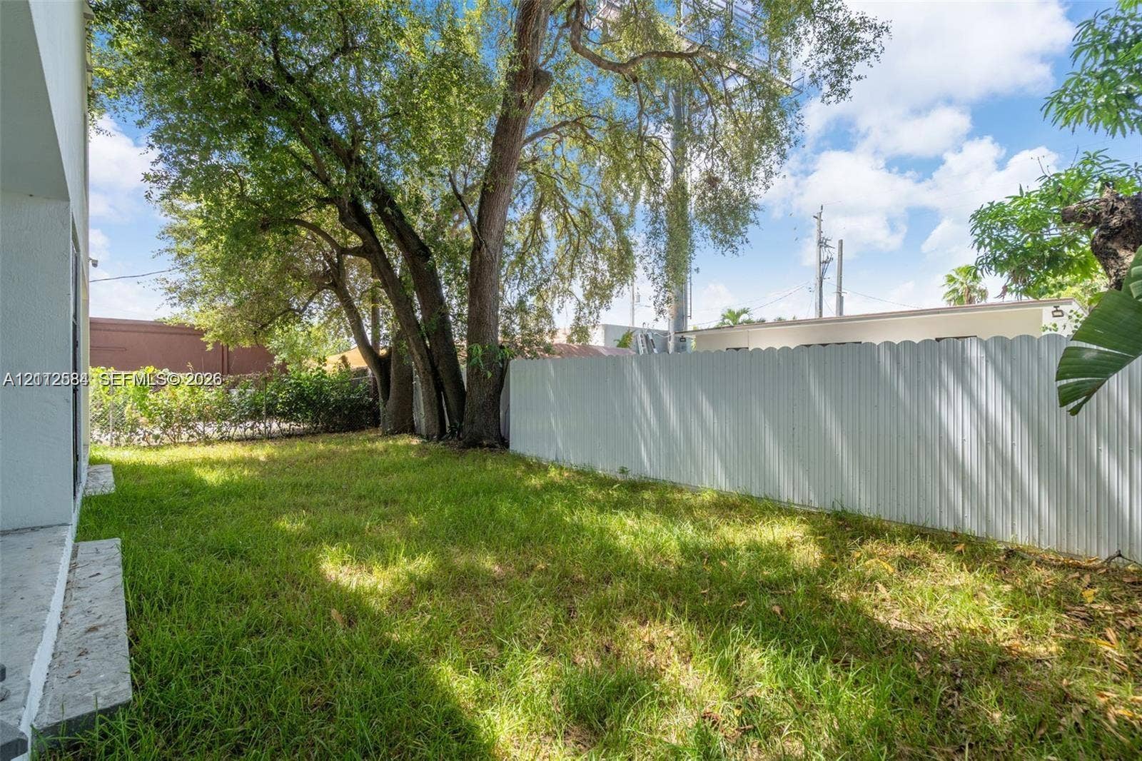 1629 NW 40th Street, Miami, FL 33142 Private backyard featuring mature trees, grass lawn, and white corrugated metal fencing