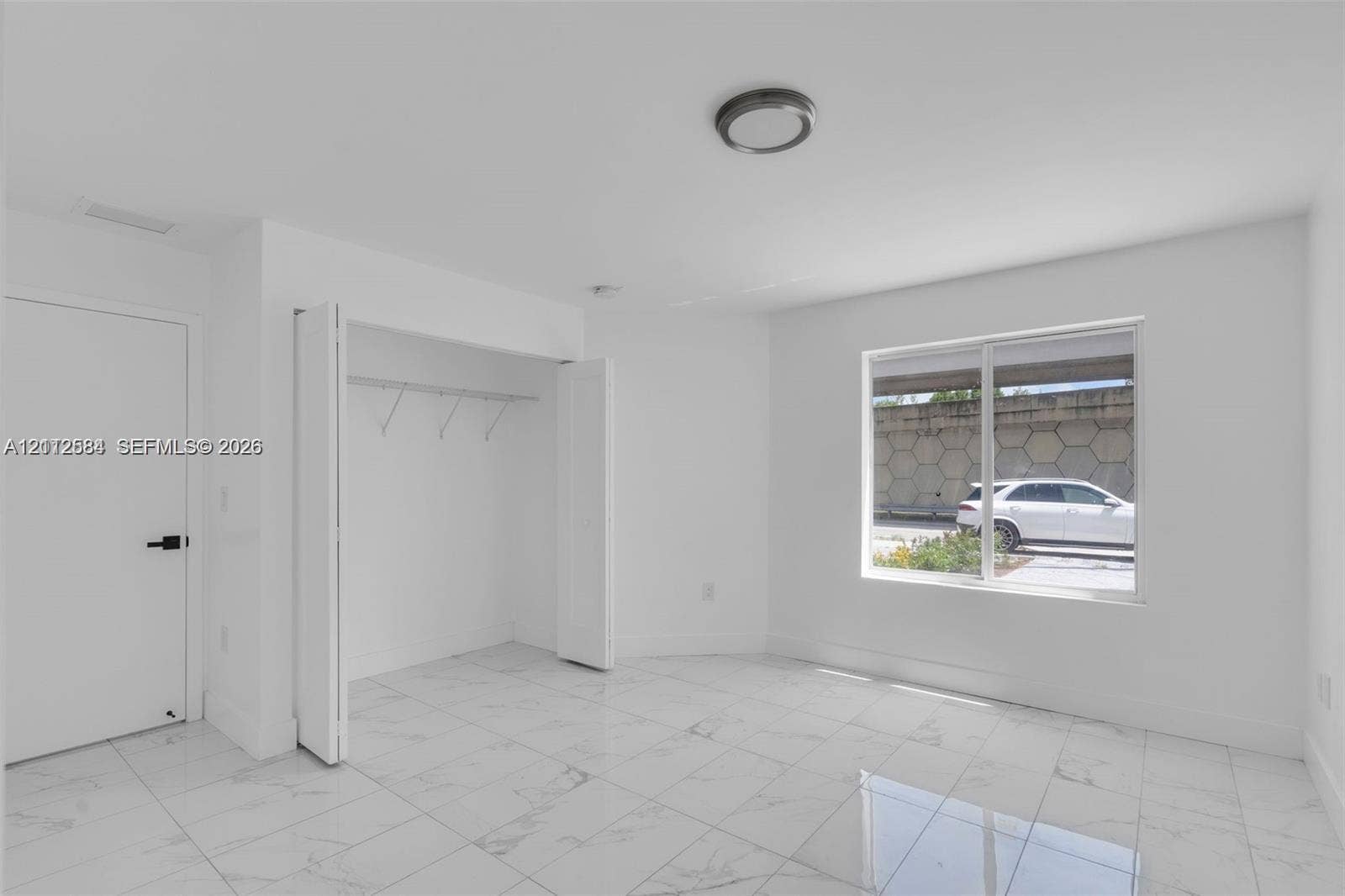1629 NW 40th Street, Miami, FL 33142 Interior space featuring neutral wall paint, large-format tile flooring, a closet with built-in shelving, and a large window
