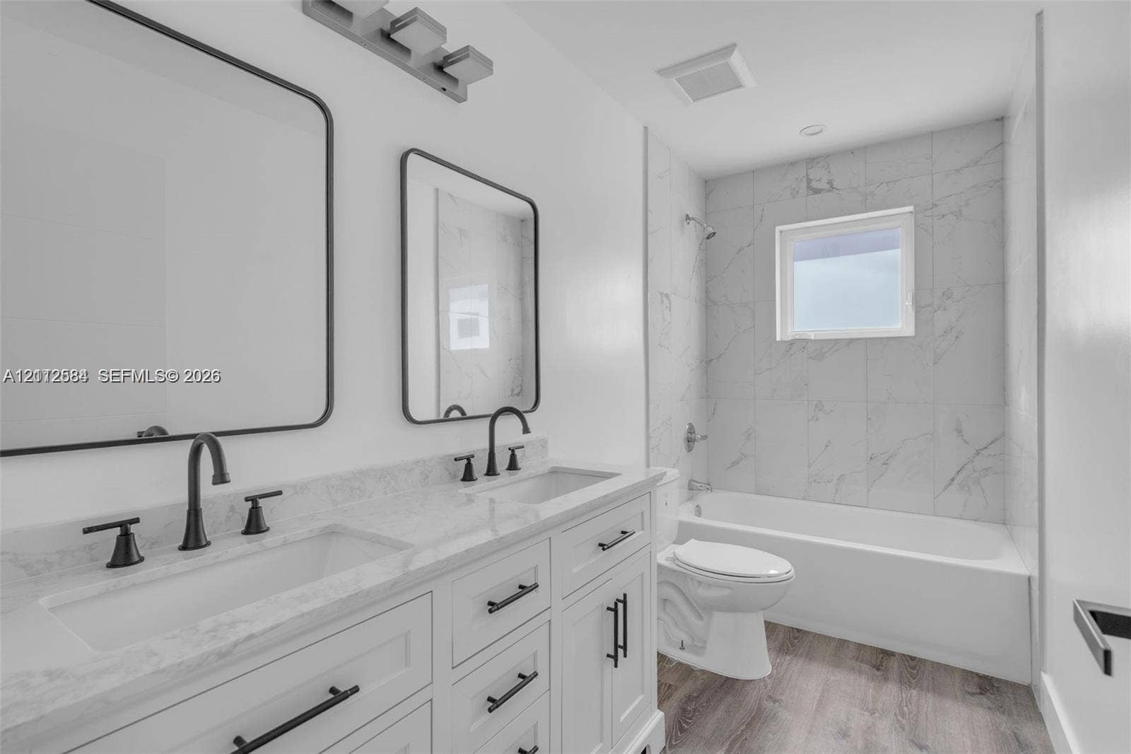 1629 NW 40th Street, Miami, FL 33142 Dual-sink vanity with stone-finish countertop, white shaker-style cabinetry, matte black hardware, dual rectangular mirrors, and a tub-shower combination featuring floor-to-ceiling tile surround