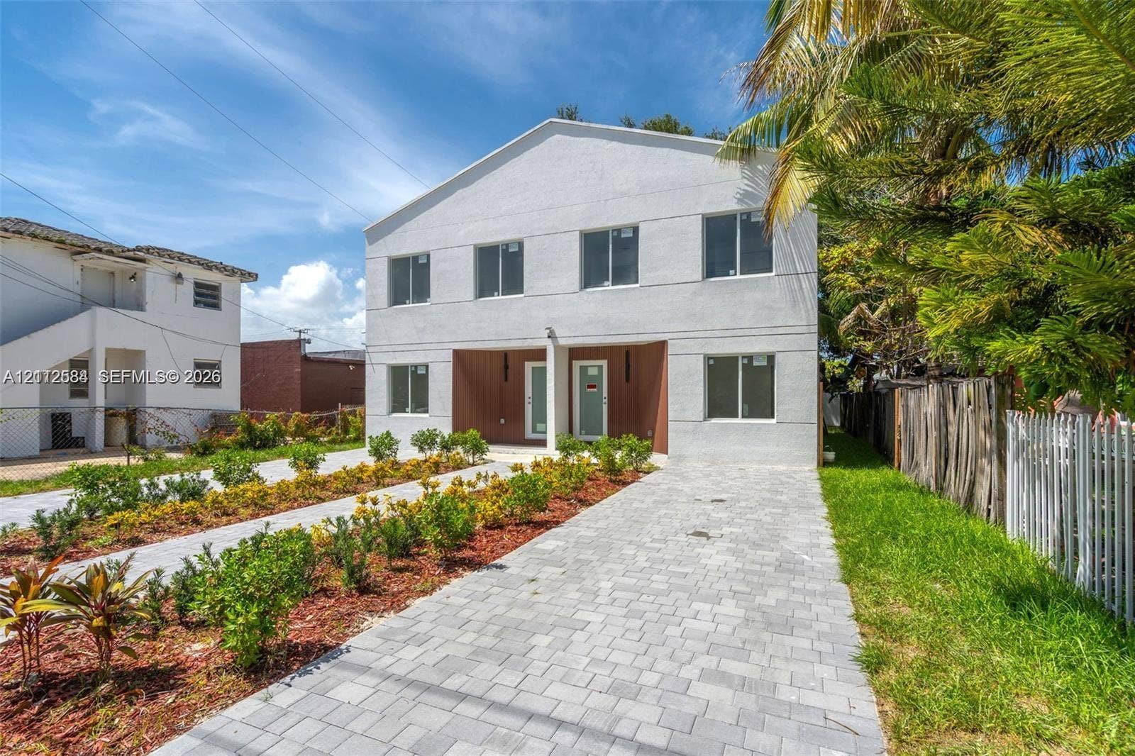 1629 NW 40th Street, Miami, FL 33142 Two-story exterior featuring a light-toned stucco facade, dual recessed entryways, rectangular windows, and a paved stone driveway