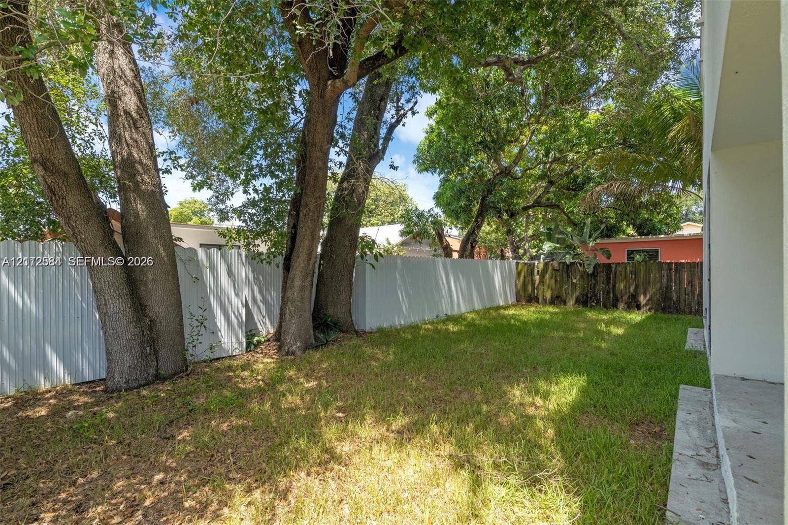 1629 NW 40th Street, Miami, FL 33142 Rear yard featuring mature trees, a concrete patio, and a white privacy fence