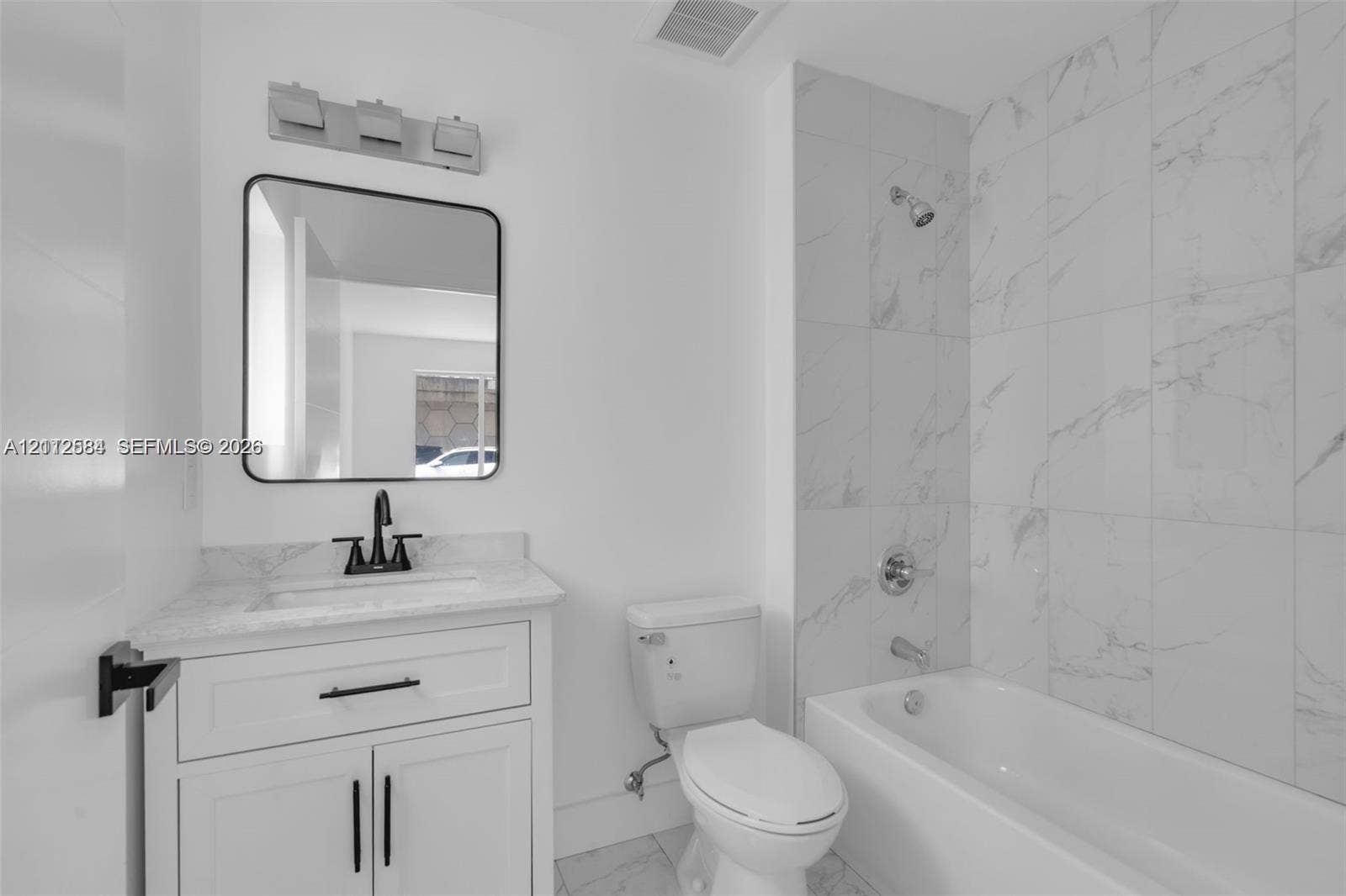 1629 NW 40th Street, Miami, FL 33142 Bathroom featuring white shaker-style cabinetry, stone-surface countertop, matte black fixtures, and floor-to-ceiling tile surrounding the tub