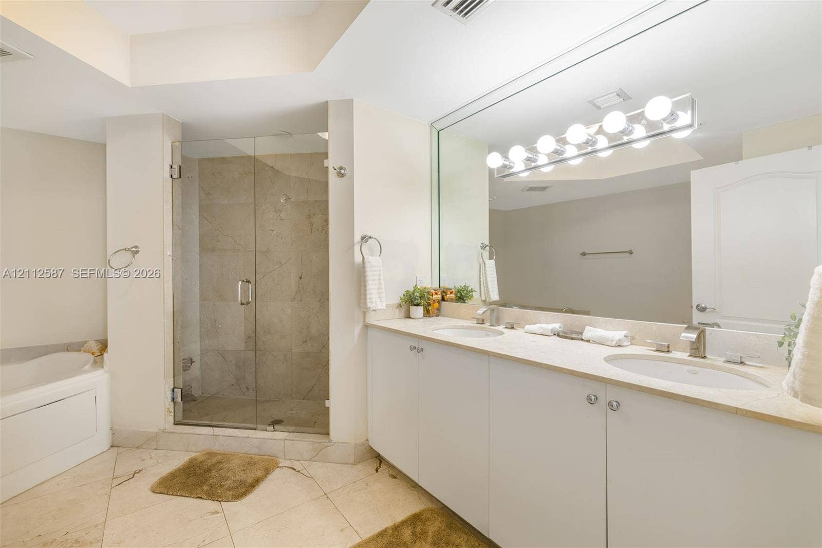 17555 NW Atlantic Boulevard, #1108, Sunny Isles Beach, FL 33160 Double vanity with integrated sinks, stone-surface countertop, glass-enclosed shower featuring tile surround, oversized wall mirror, and soaking tub