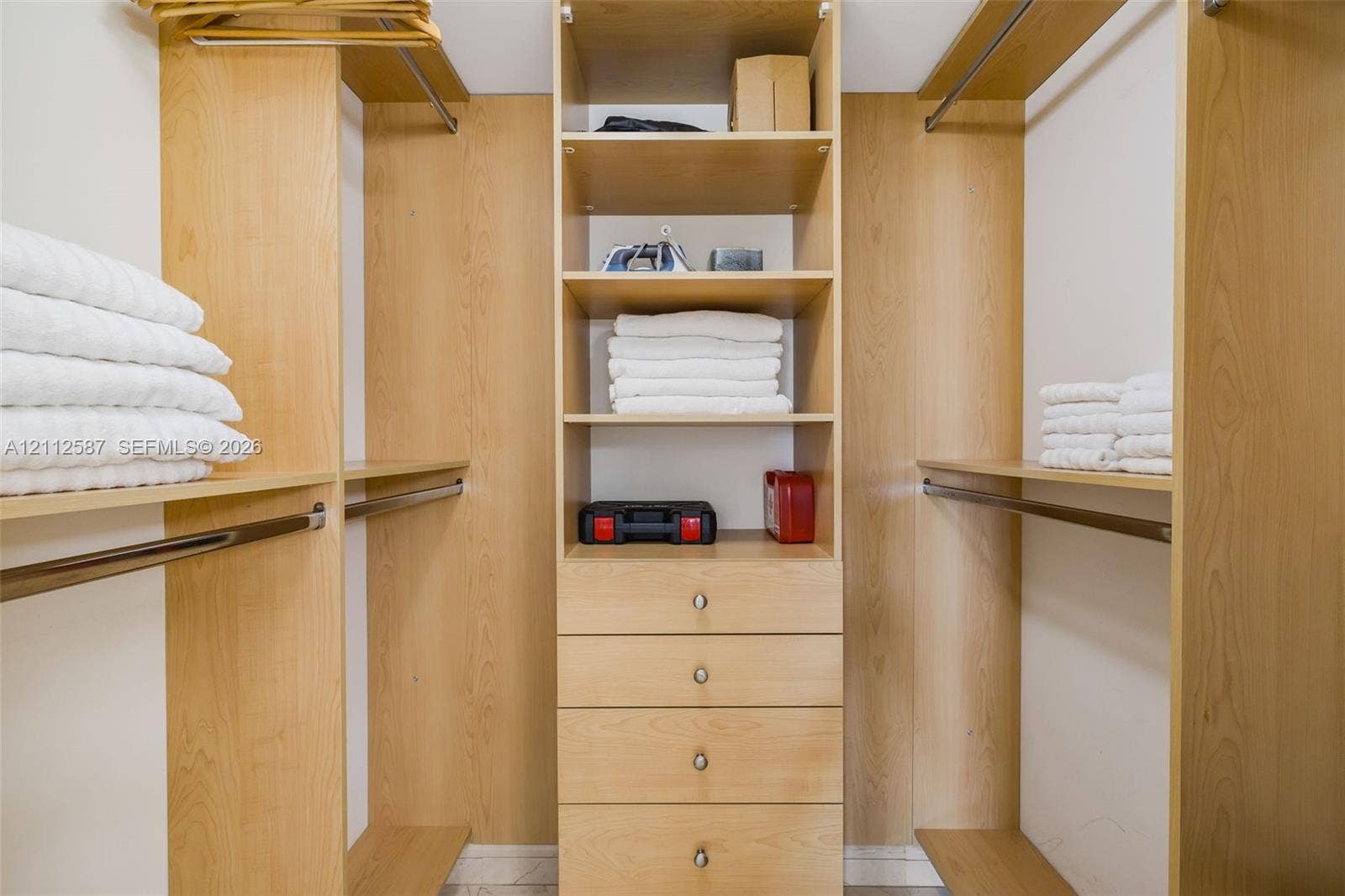 17555 NW Atlantic Boulevard, #1108, Sunny Isles Beach, FL 33160 Customized closet organization system featuring light wood-finish shelving, integrated hanging rods, and a center stack of four built-in drawers