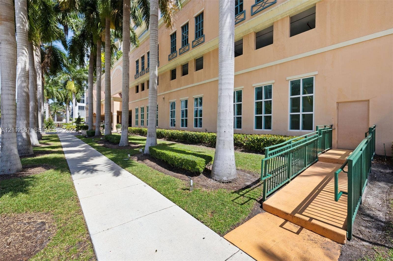 17555 NW Atlantic Boulevard, #1108, Sunny Isles Beach, FL 33160 Exterior facade featuring multi-story stucco construction, manicured landscaping with mature palm trees, multi-pane windows, and a dedicated ramp with metal handrails