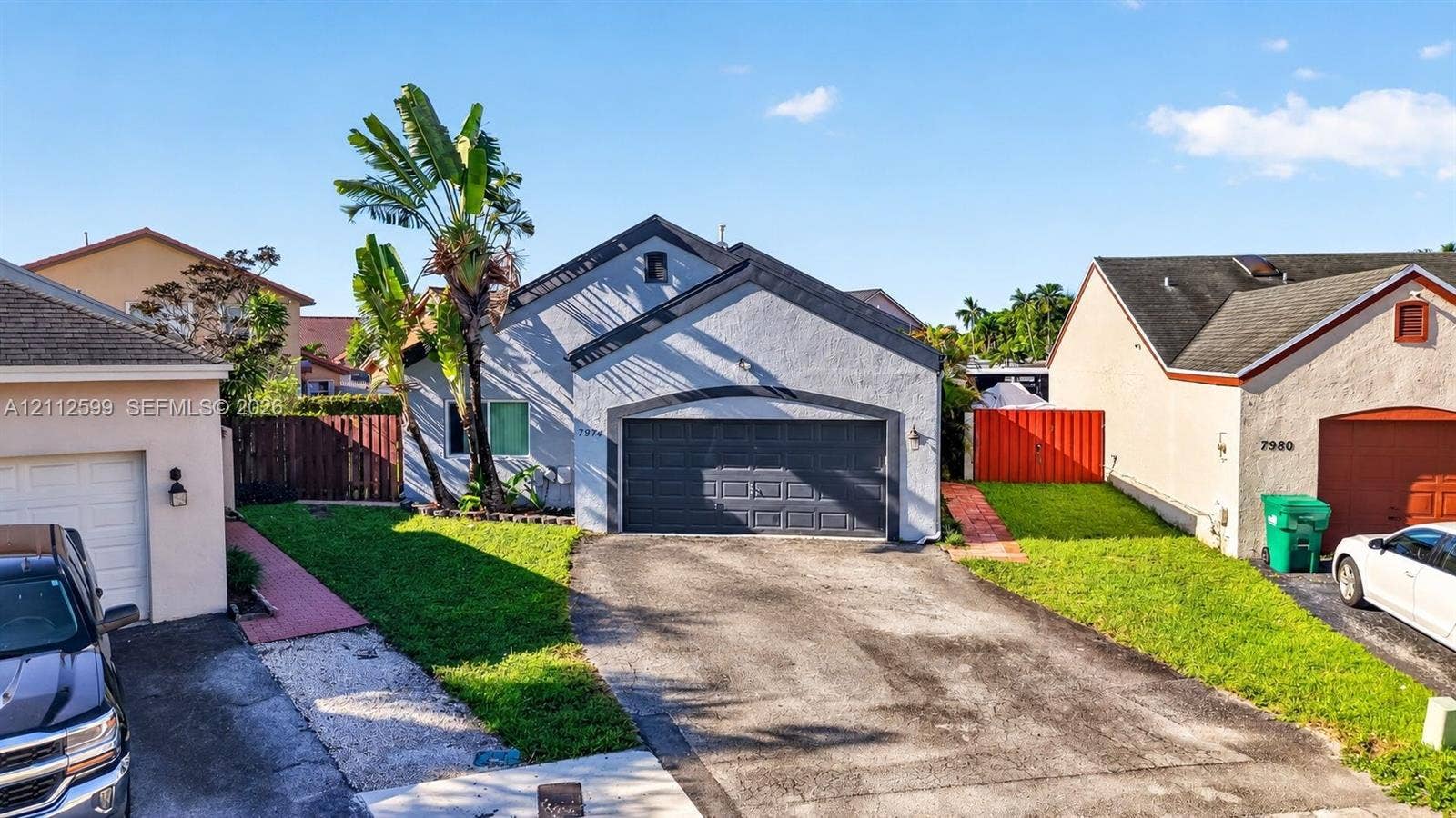 7974 NW 190th Terrace, Hialeah, FL 33015 Stucco exterior residence featuring an asphalt shingle roof, a two-car garage, an asphalt driveway, and mature landscaping